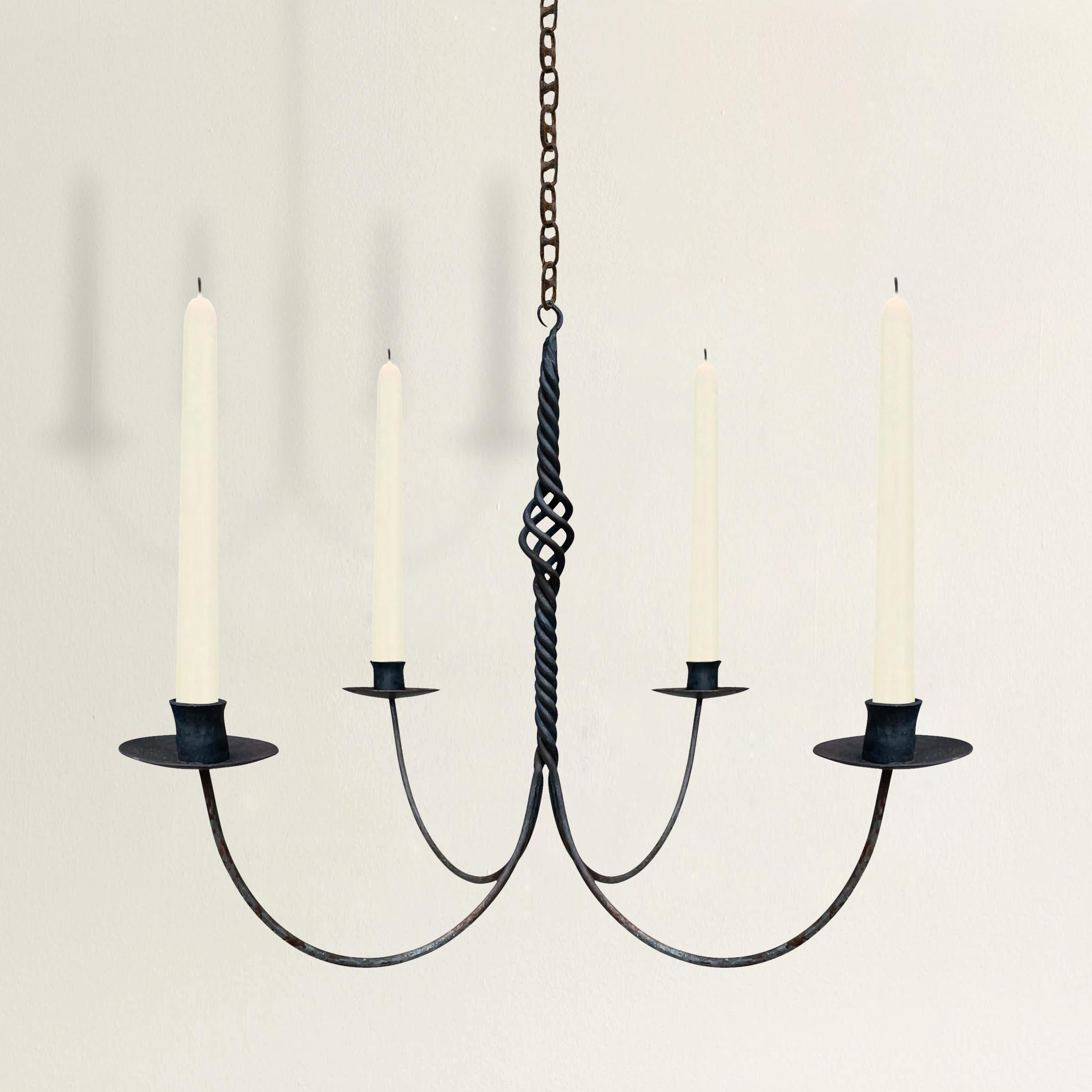 A quaint 19th century American hand-wrought iron chandelier with four arms, each with long curved arms projecting from a central twisted iron down rod with an open spiral design element in the center. Not electrified.