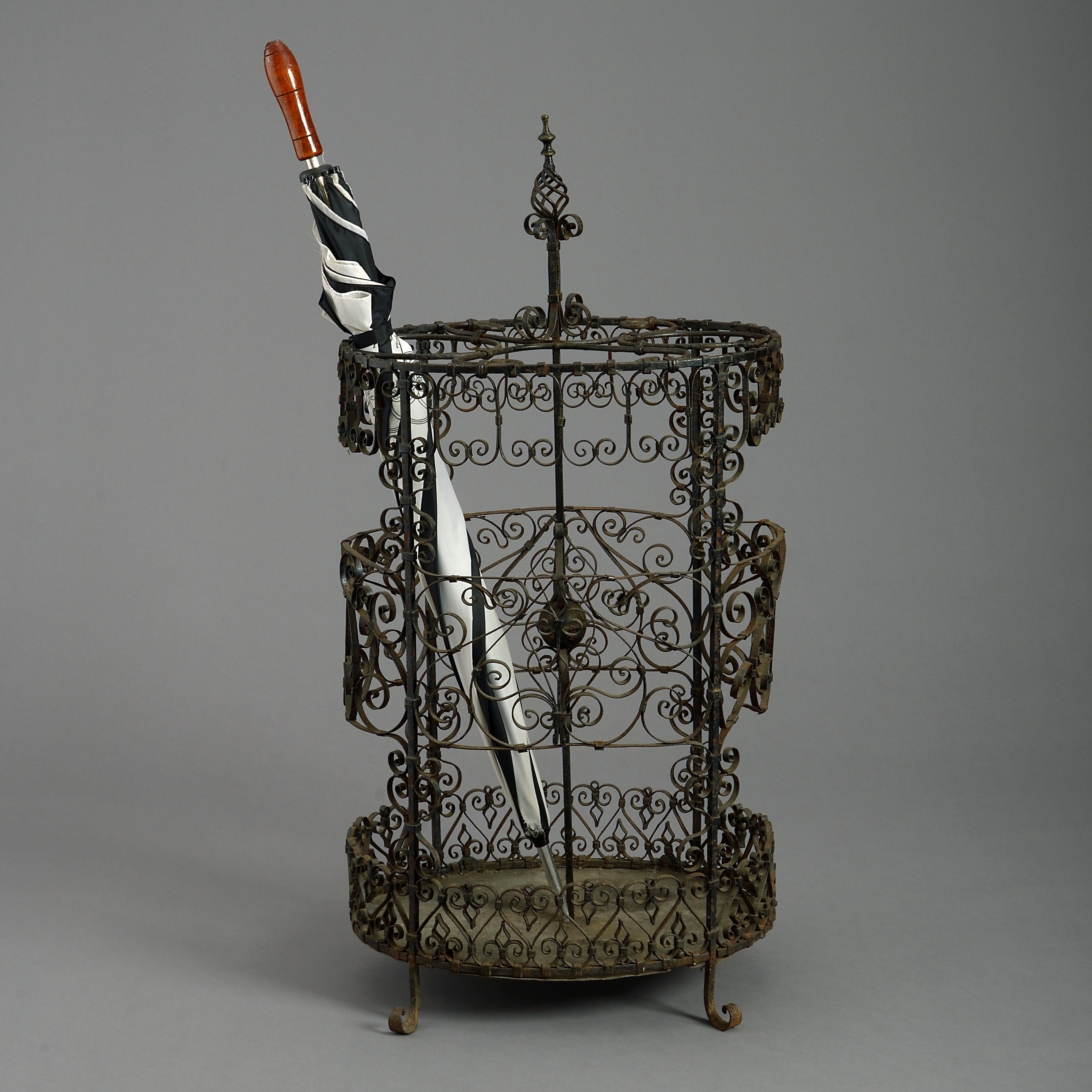 A rare and intricate mid-19th century wrought iron stick or umbrella stand, the central swirl finial support surrounded by a cage of elaborate scrollwork, all raised on four scrolling feet.