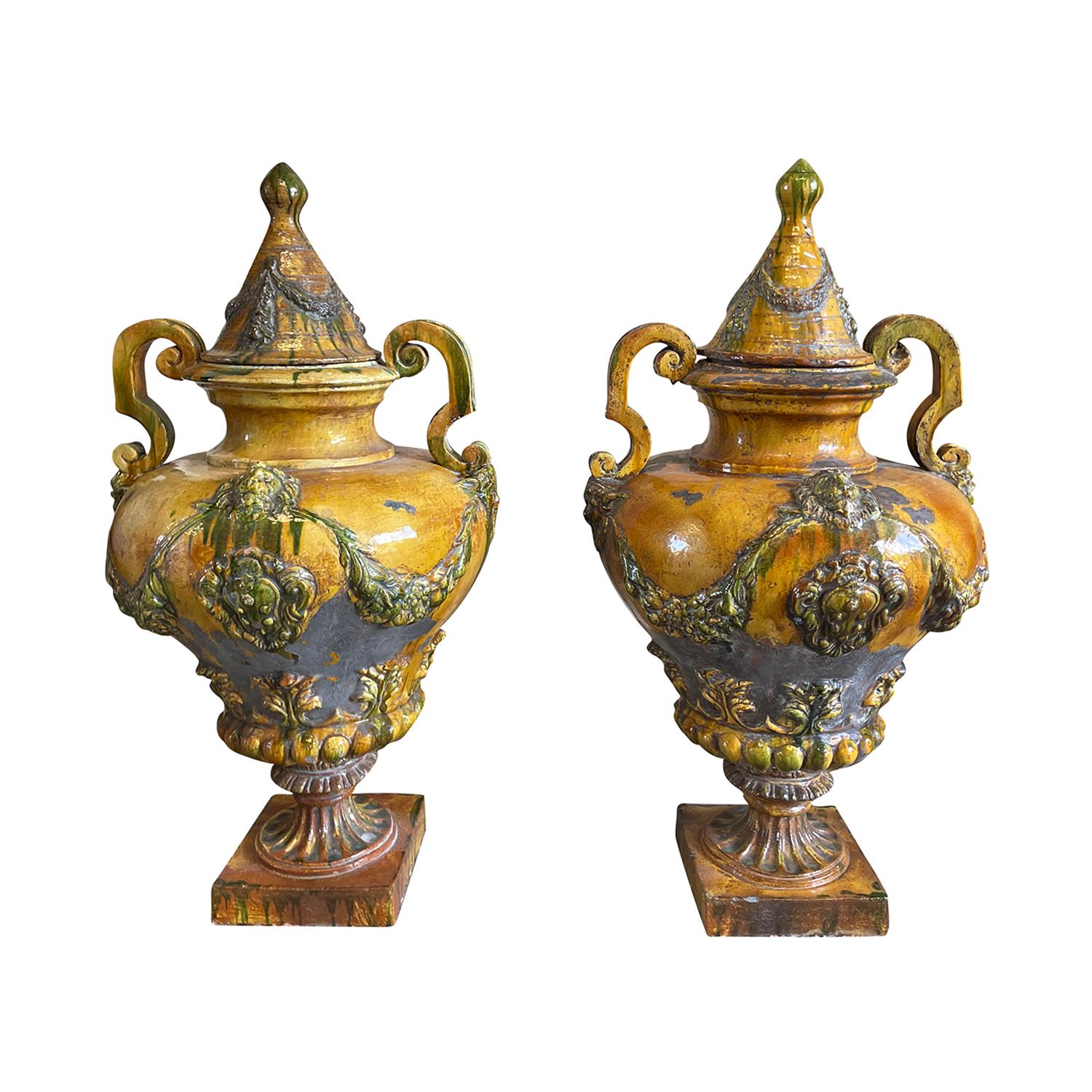 A pair of antique Italian double-handled baluster urns made of ceramic glazed in the 18th Century style in a warm honey yellow glaze with green accents, in good condition. These decorative garden ornaments are raised onto a square base. Wear