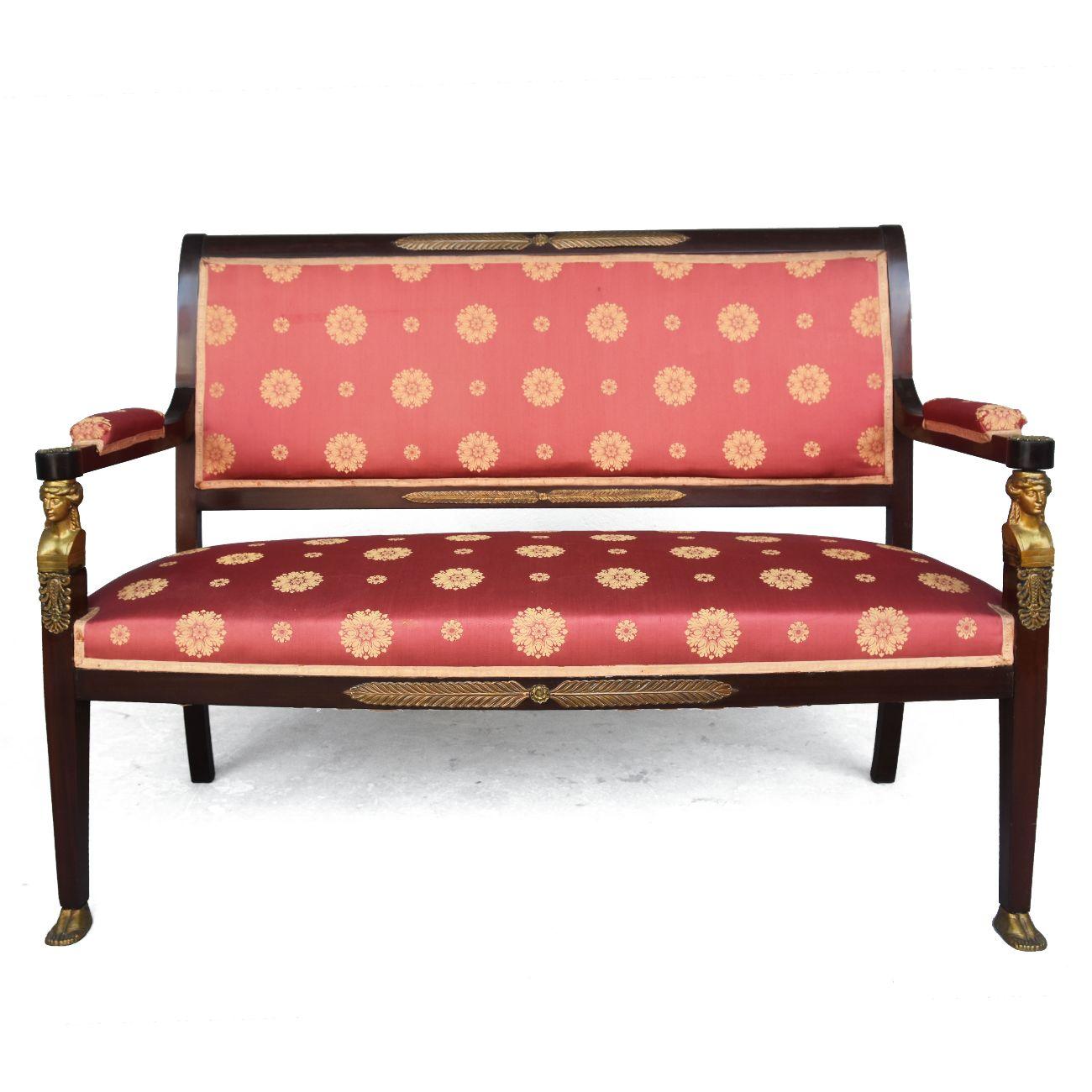 salon de style 19e Empire en acajou et bronze doré à têtes de cariatides et pieds griffes. Banc, deux fauteuils, deux chaises. Période 19ème siècle. Tapisserie à restaurer. Fauteuil 98 cm H x 60 cm L x 63 cm P. Banc de 97 cm de haut x 130 cm de