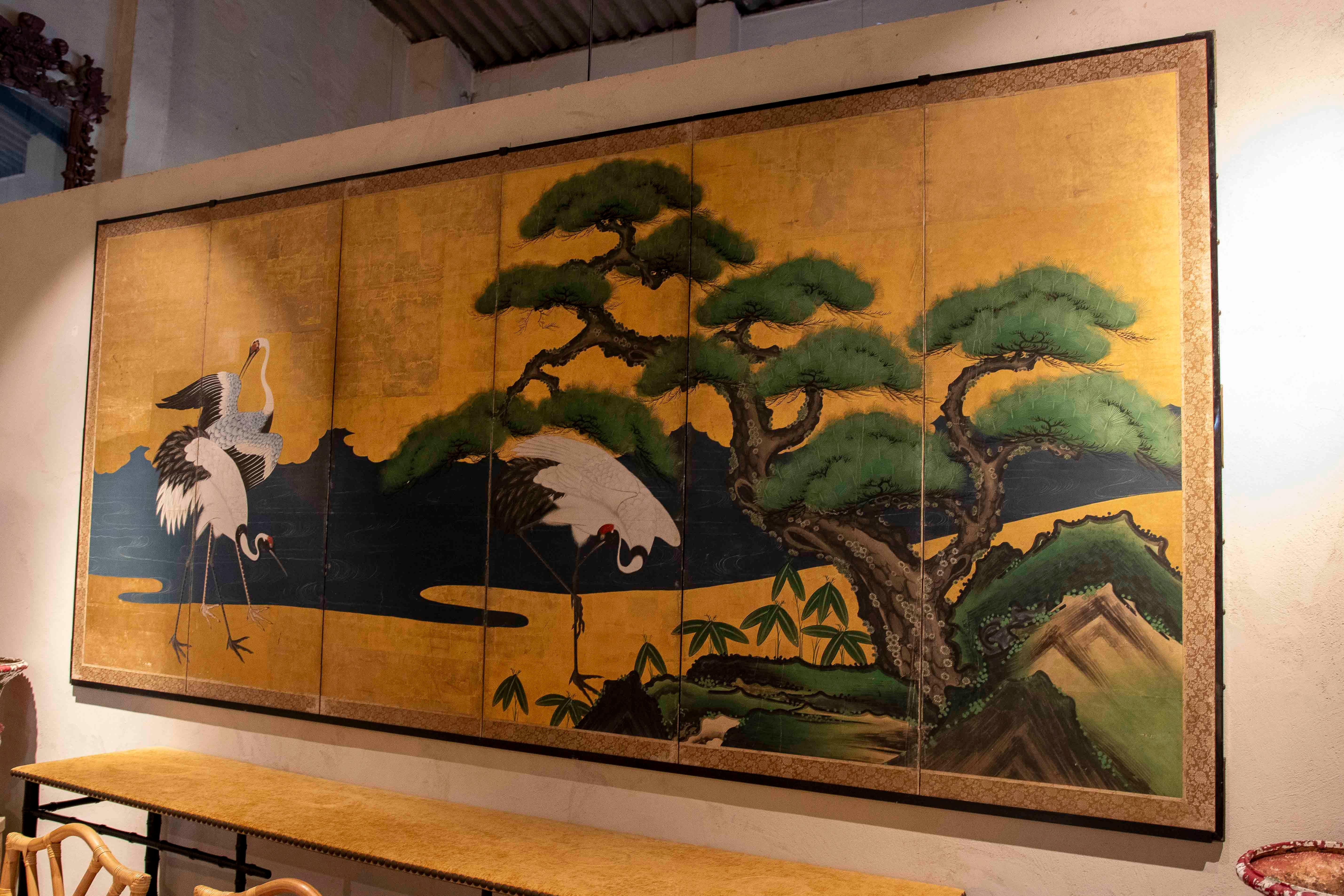 Stunning four-panel Japanese screen decorated with a traditional scene of cranes and a majestic pine tree on a gold background. The painting technique highlights the details of the birds and the tree, symbolizing longevity and prosperity in Japanese