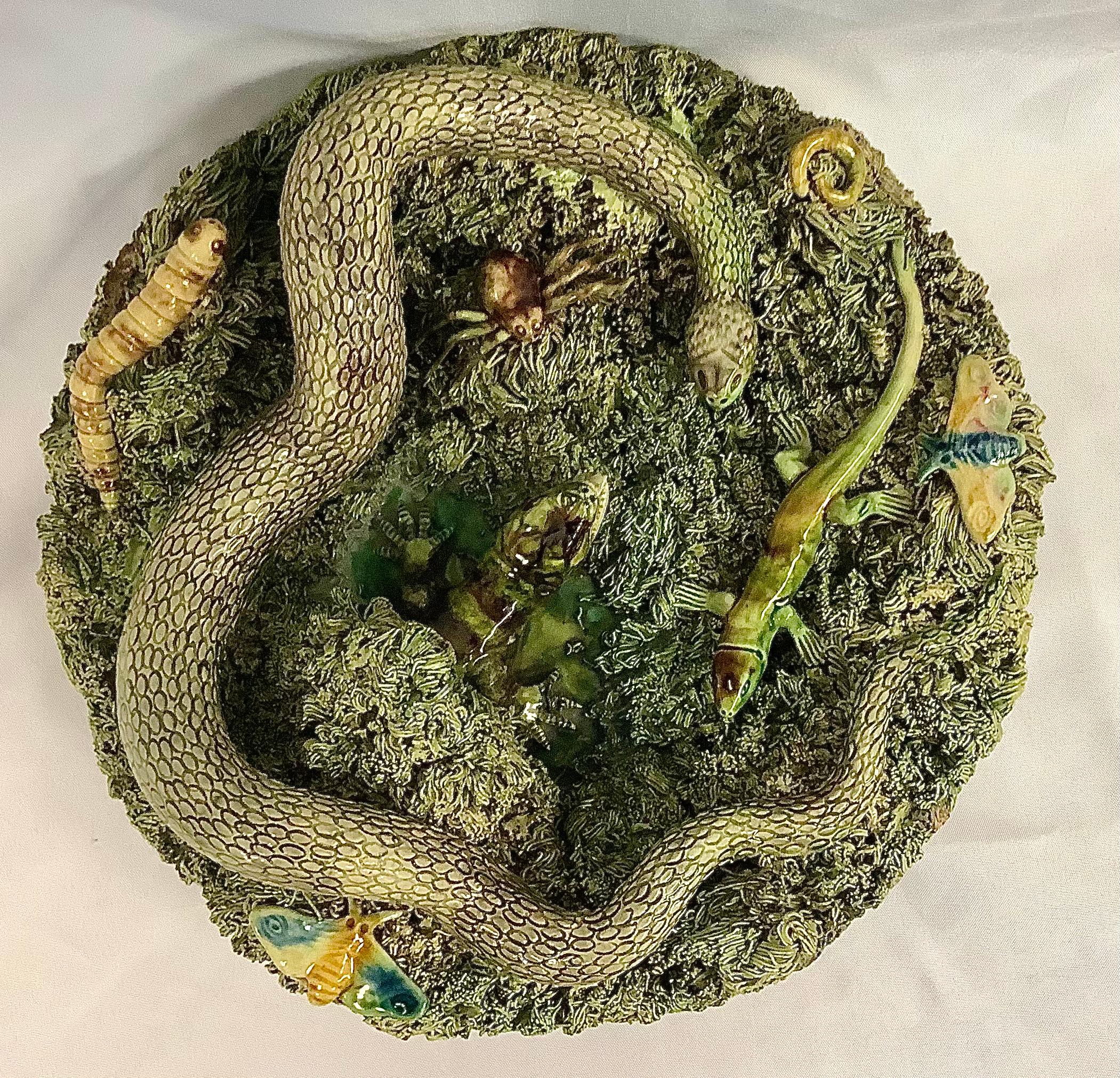 Ancienne assiette de style Palissy en majolique portugaise du XIXe siècle. L'assiette est centrée sur un grand serpent et un grand lézard, avec un ver, une chenille, un papillon et un lézard entourés d'une touffe d'herbe brune et verte. A signé Jose