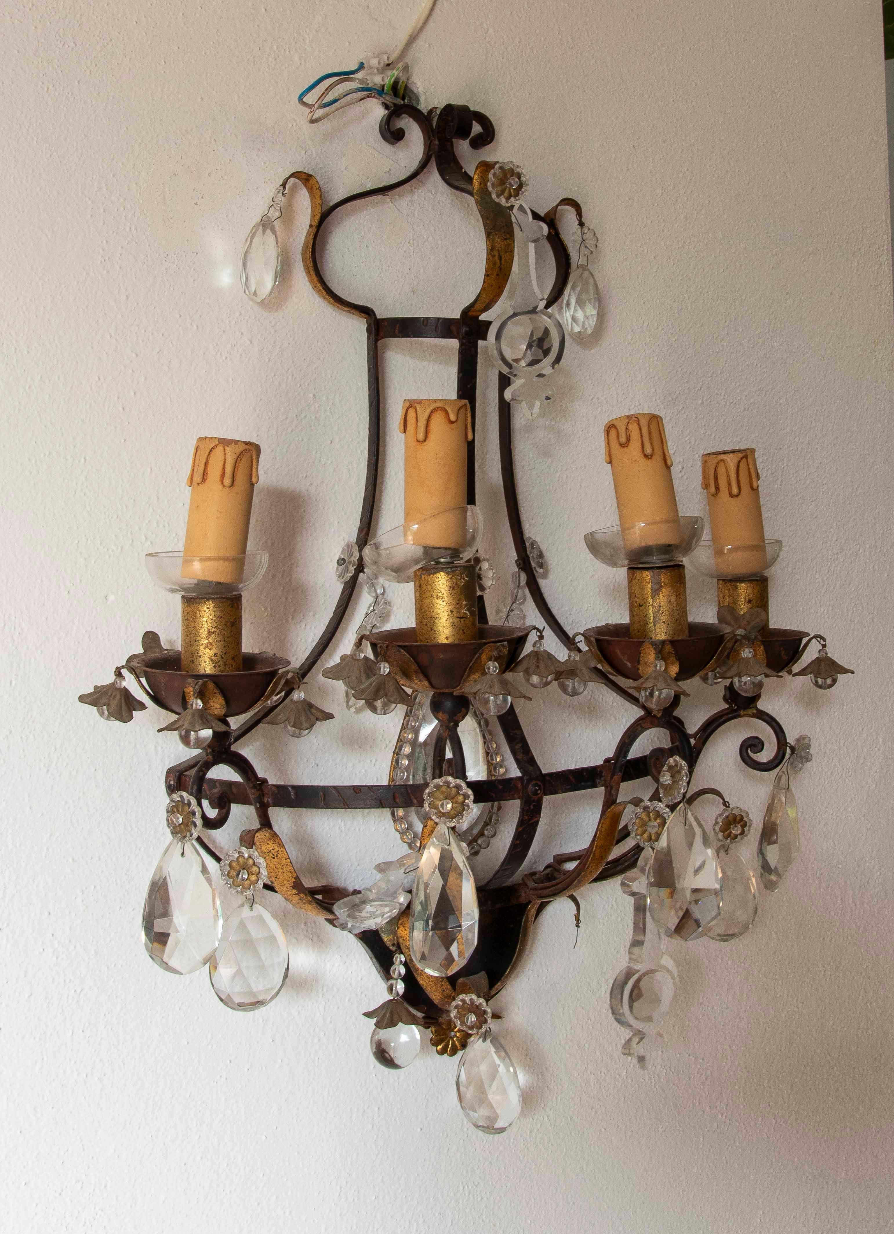This elegant pair of wrought iron wall sconces showcases a classic design, distinguished by their symmetrical structure, each with five candle-holder arms. The piece features an antiqued bronze and gold finish, highlighting its historic and