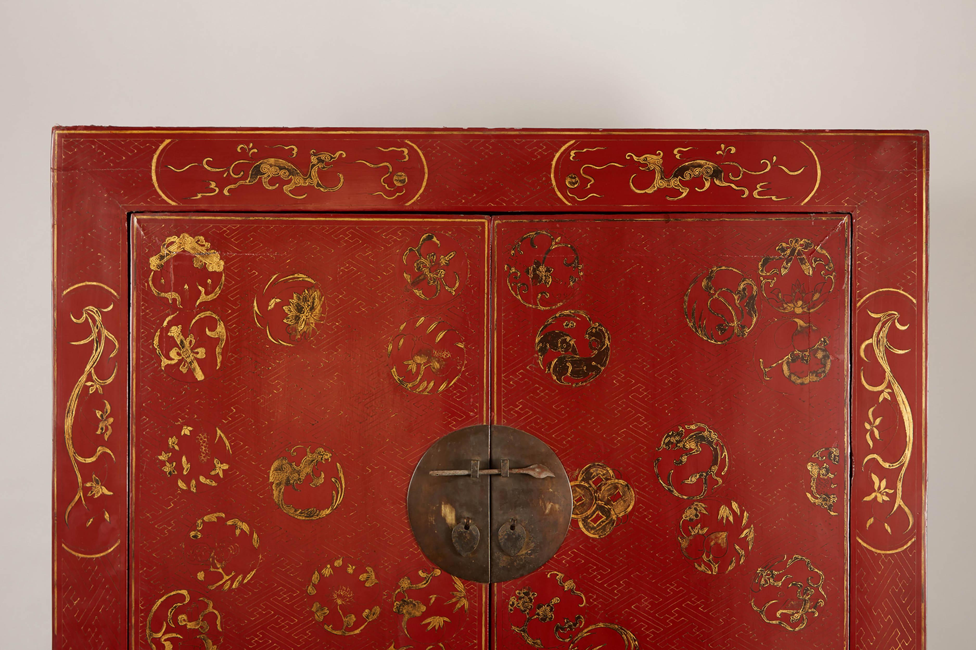 Ce meuble chinois du XIXe siècle est de conception simple et présente une plaque frontale ronde avec des boutons percés et des poignées en métal, un tablier et un tympan à tête de tablier. L'armoire est peinte en rouge avec des motifs peints en or.