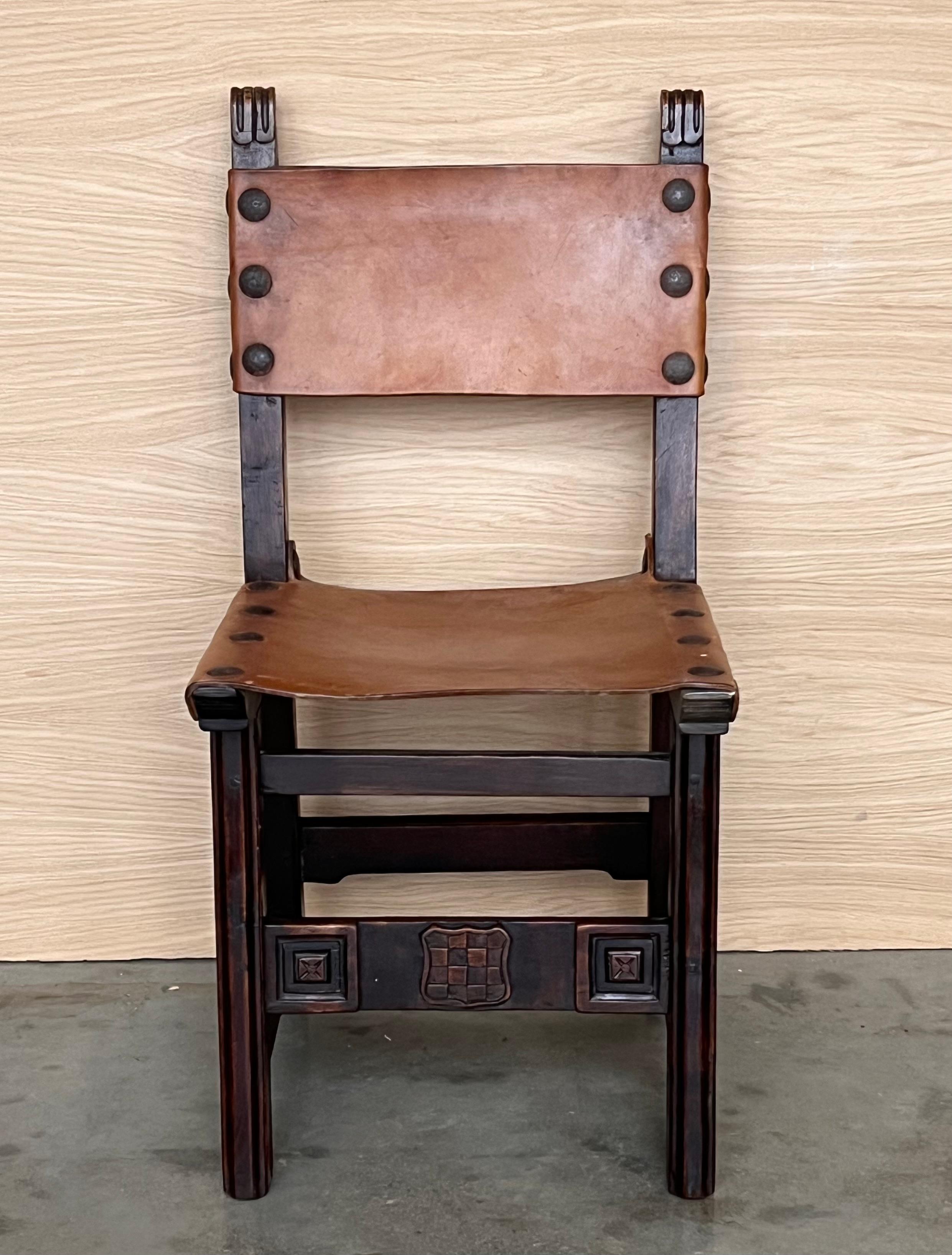 A set of 6 Spanish chairs with leather sling seatsand backs on oak and sycamore frames with hand carved decoration. These chairs are true to the Spanish character and each features carvings that employ typical Spanish elements. The leather sling