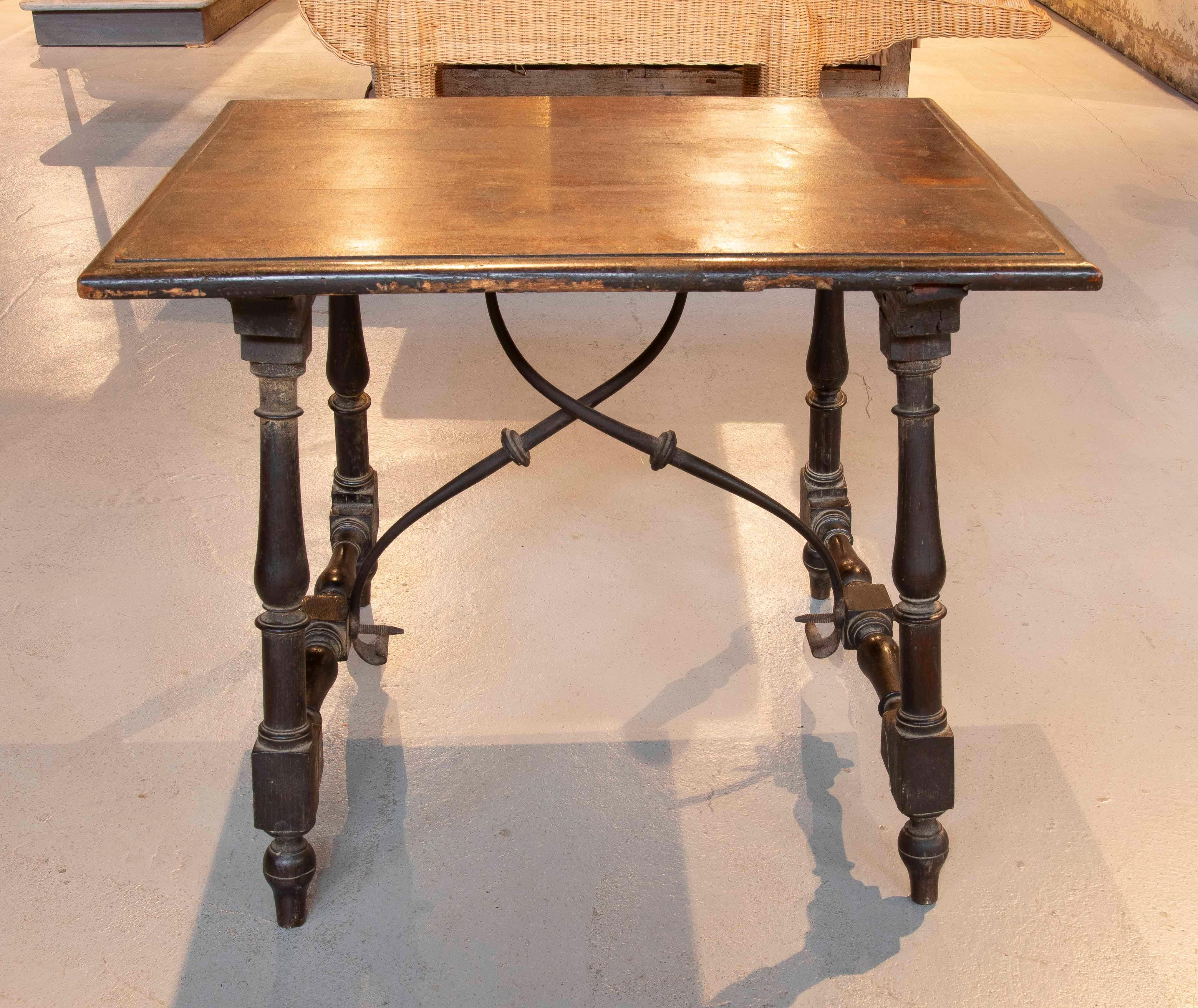 Elegant Spanish-inspired side table with a rectangular top in solid wood in a warm, dark tone. The base is composed of turned legs joined by wrought iron crossbars with a crisscross design and decorative details that provide stability and a
