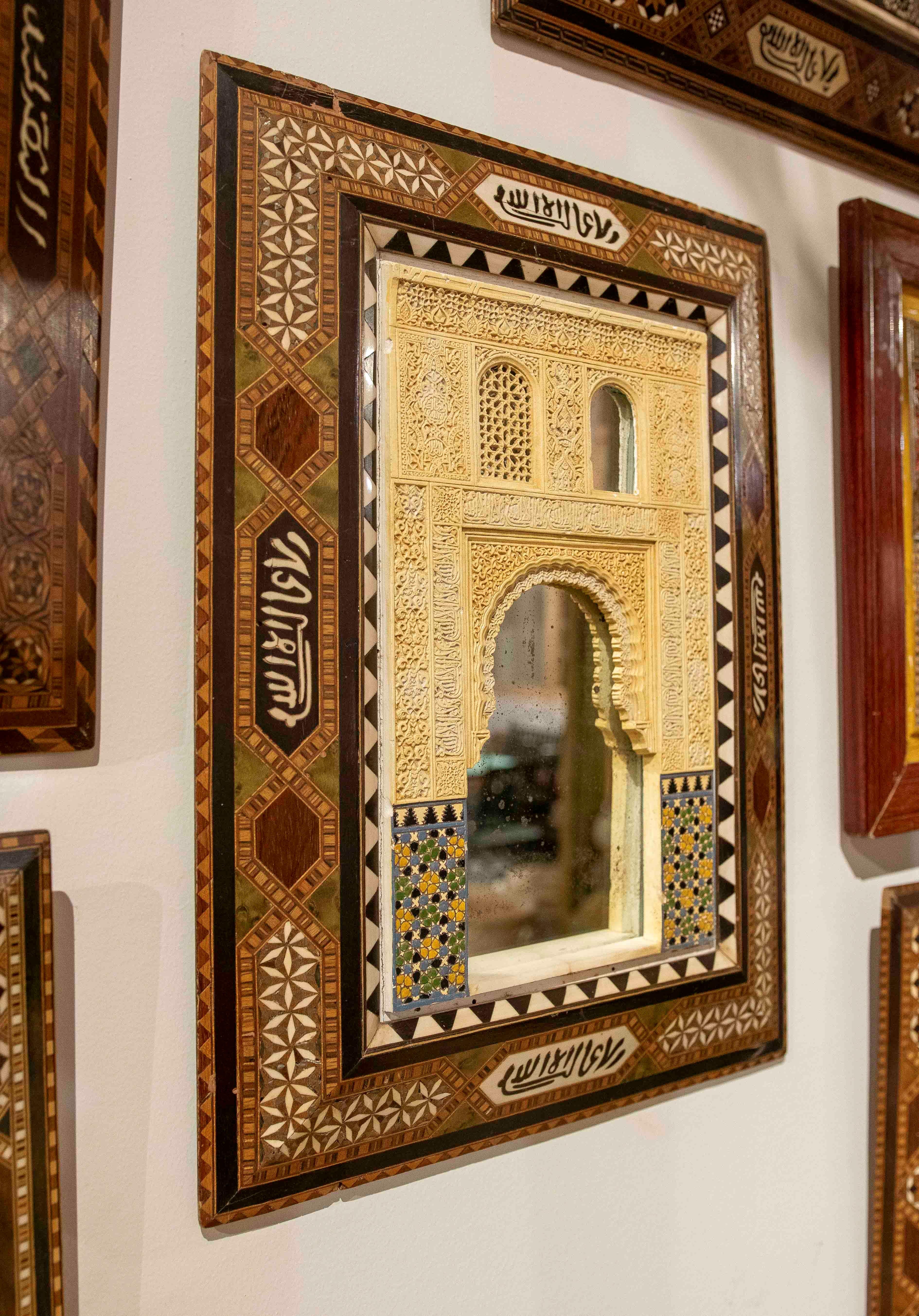 Un beau modèle décoratif inspiré de l'architecture nasride de l'Alhambra de Grenade. La pièce présente un arc en fer à cheval richement sculpté en stuc peint à l'ivoire, accompagné d'inscriptions arabes et de mosaïques géométriques dans la partie