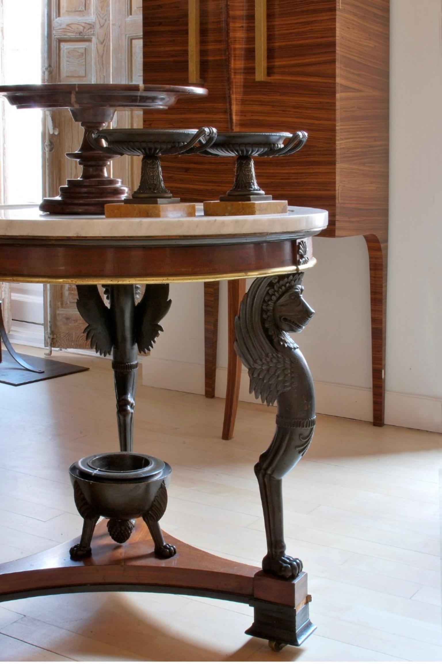 Gueridón  table with marble top from the Empire period, Swedish work from the early 19th century, in cherry wood and ebonized wood, the top is supported on winged lions and a triangular base with a cup in the center, it is topped by wheels covered