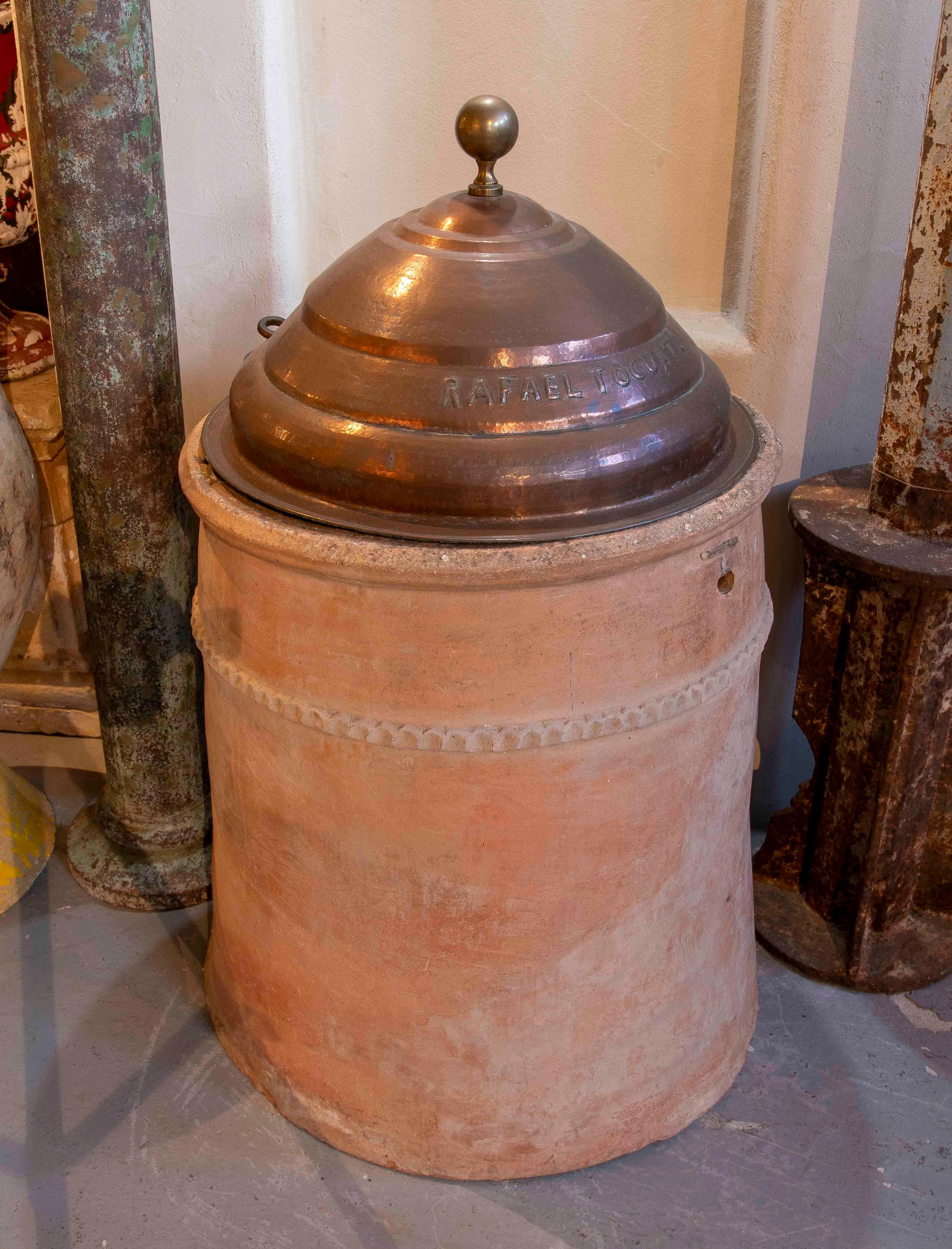 Terracotta well spout with an elegant copper lid engraved with the name ‘Rafael Tocuato’. The terracotta base has a rustic and natural design, with embossed details around the rim that emphasise its handcrafted character. The copper lid, with a