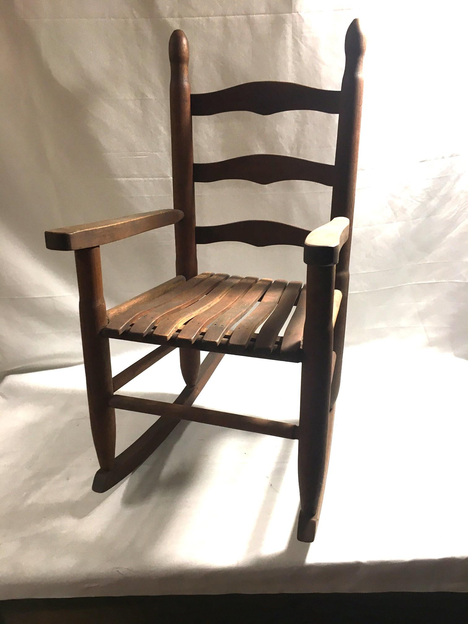 Questa robusta sedia a dondolo antica in rovere per bambini conserva la vernice originale color rovere miele e la seduta a doghe. Una bella patina antica. 
