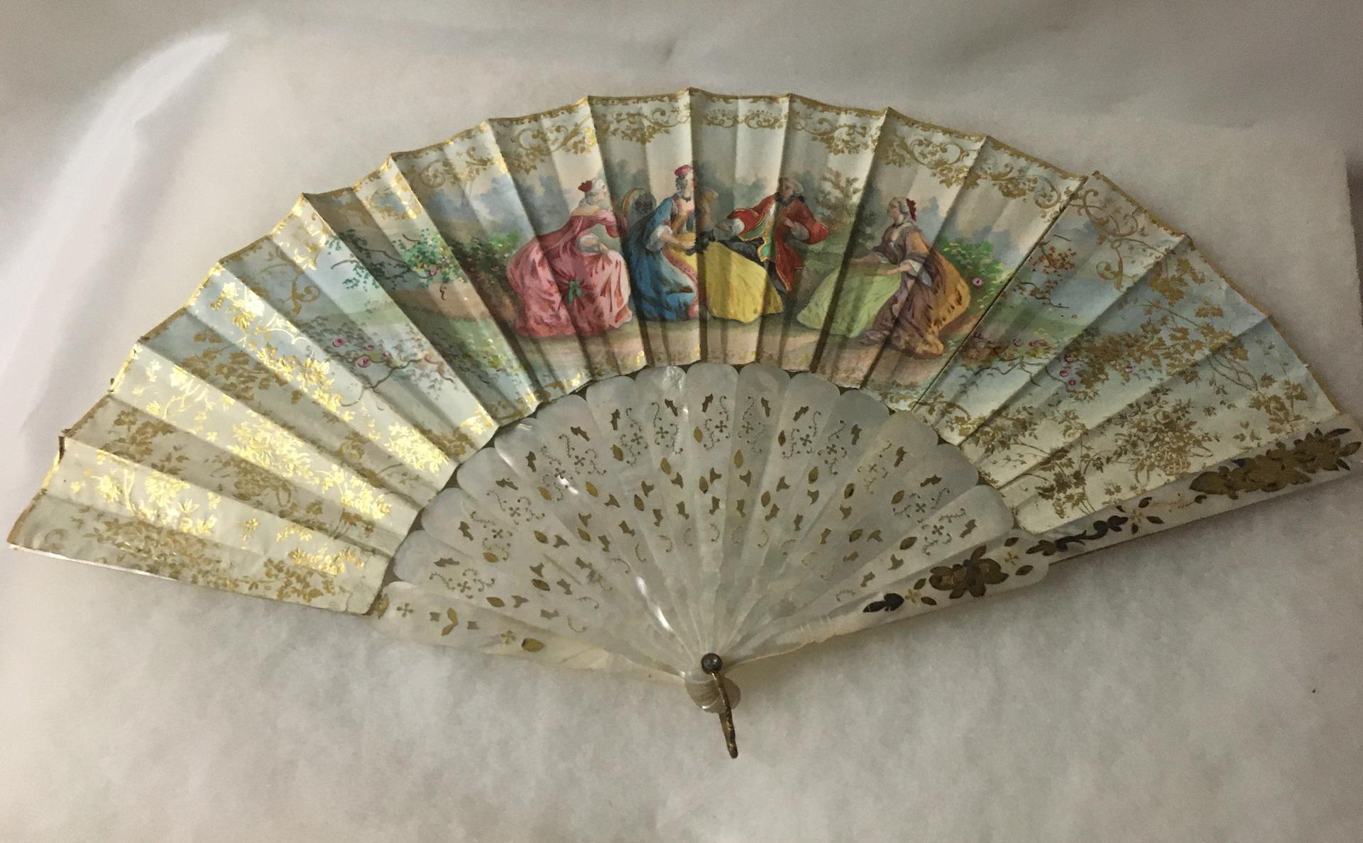 This splendid highly decorative, colorful double sided fan is beautifully hand-painted and on the front side features stunning figures dressed in French Court attire. The background is a charming classical outdoor scene with a pavilion and cherub