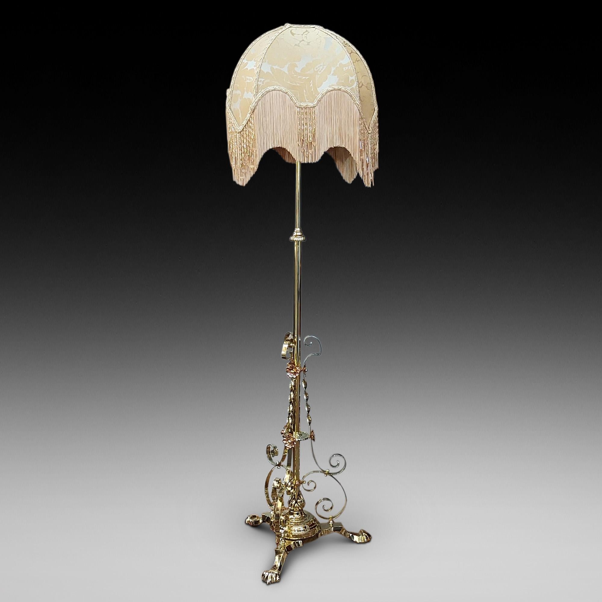 19thC Arts and Crafts adjustable brass standard oil lamp, extendable shaft supported by a triform base with scrolling limbs and copper floral decoration - - converted to electric - 22