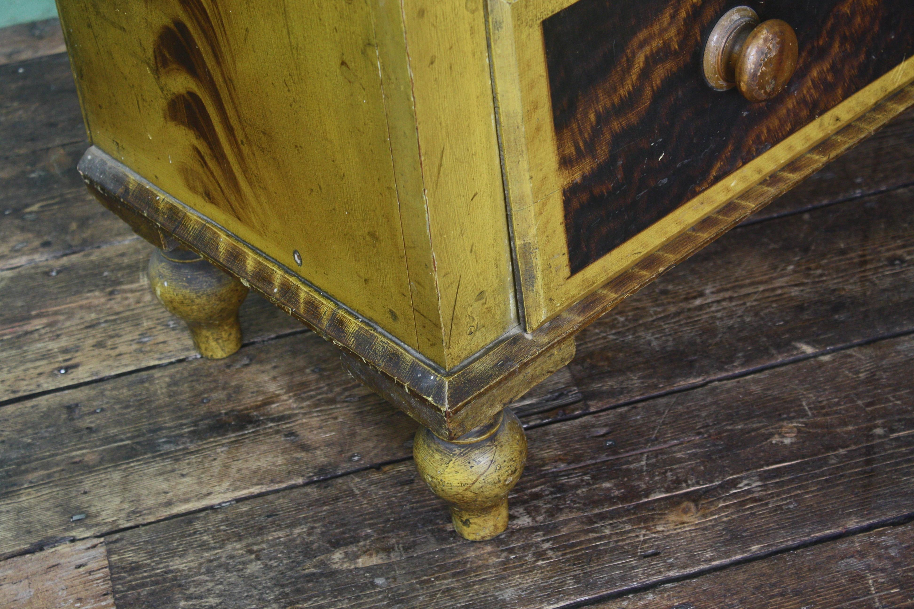 A early Victorian 19th century Scottish chest of drawers of diminutive proportion. Comprising of two short and two long drawers. A rectangular chamfered top with a decorative brown grained finish on mustard yellow ground. The drawers terminate on