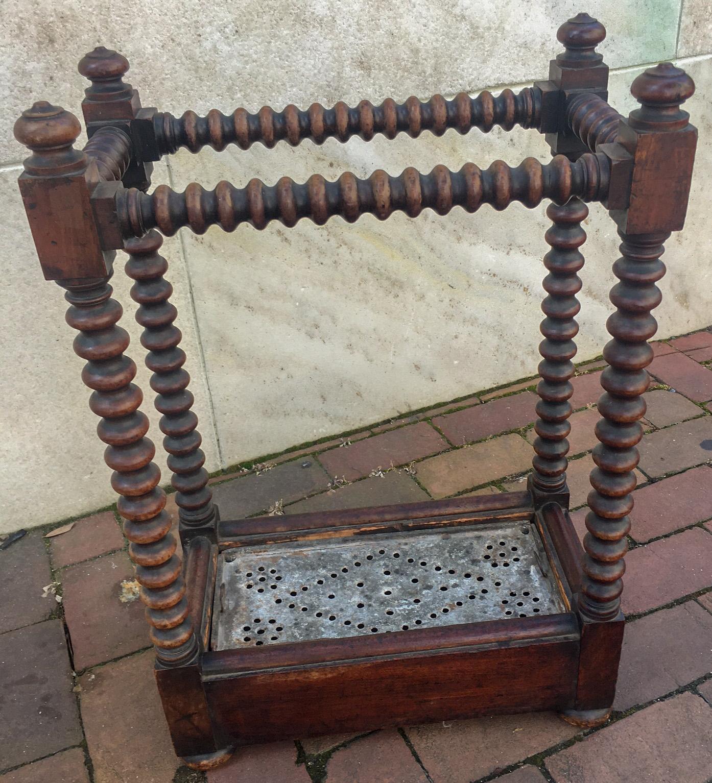 This petite sized oak umbrella stand features spool turned legs and sides, with carved finials at the top, bun feet and a galvanize metal removable drip pan. 
