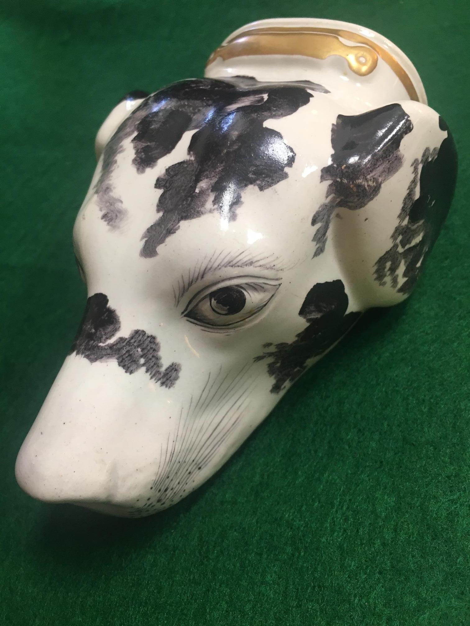 
 This charming fellow is an English porcelain stirrup cup in the form of a large hound's head. He is very detailed including naturalistically modelled features, white and black markings, recessed eyelids, a red mouth, wispy whiskers and ears