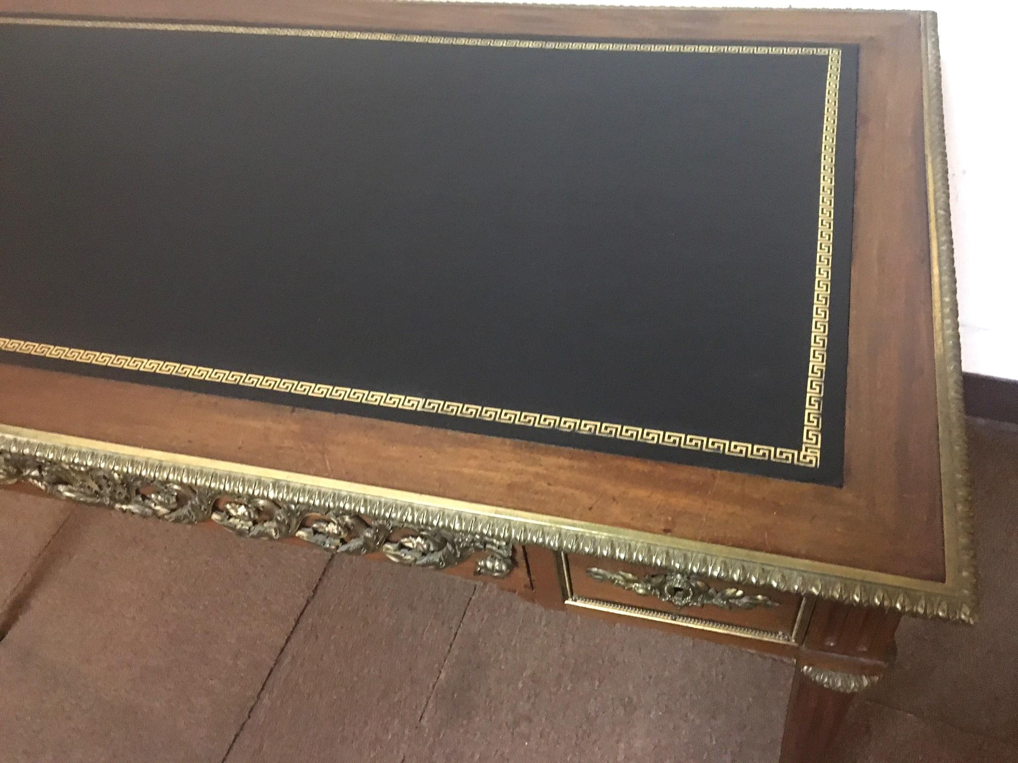 Handsome diminutive size French Louis XVI lady's writing table constructed of mahogany and featuring a black leather top with gold Greek key border, foliate bronze ormolu mounts and turned fluted legs. There are three drawers, one large in the