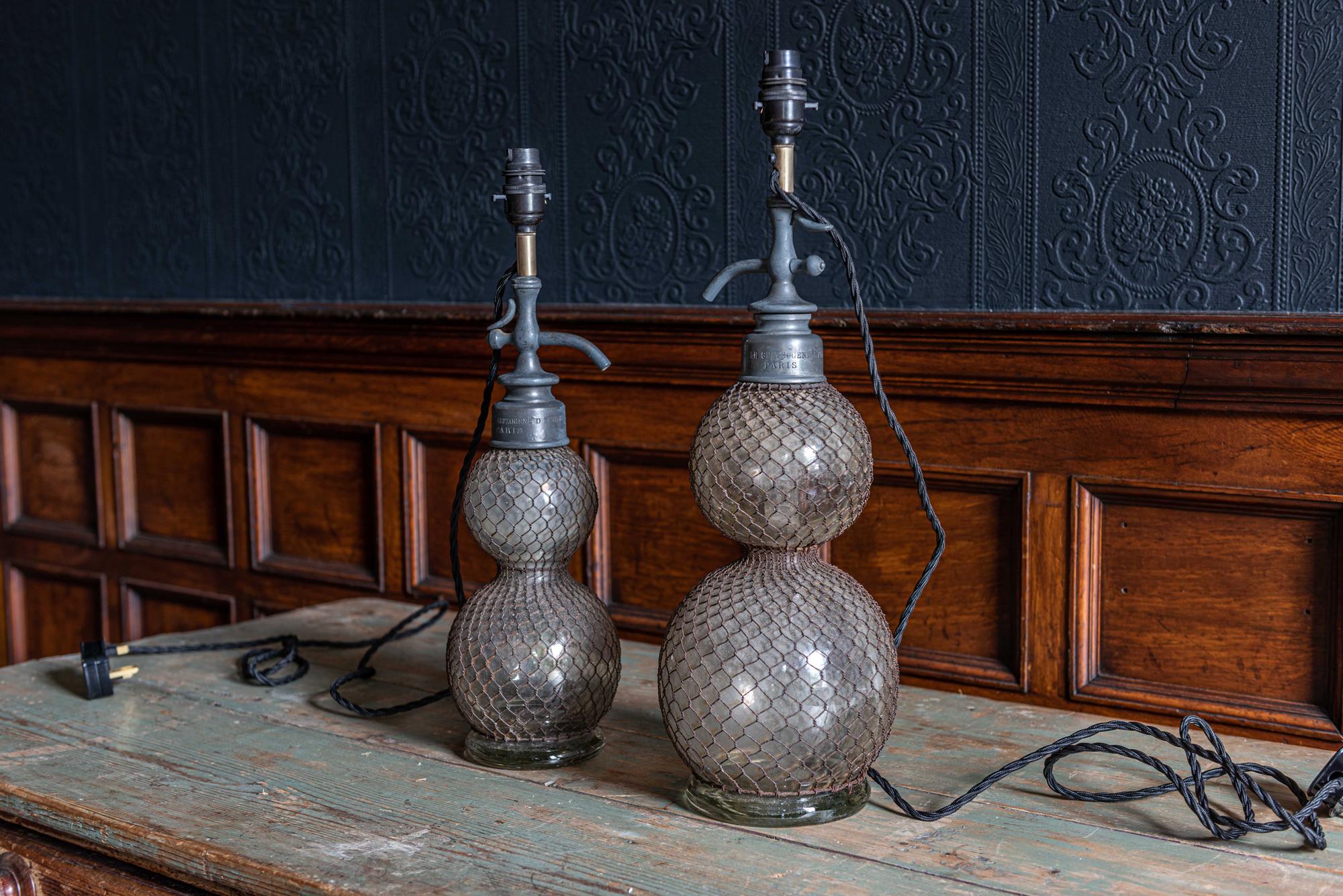 19th century French seltzer siphon lamps
Parisian hand blown glass 'double ball' seltzer or soda siphons covered in decorative wired jackets. Paris makers name engraved on the pewter neck, sourced from Paris.

The large lamp has two large cracks but