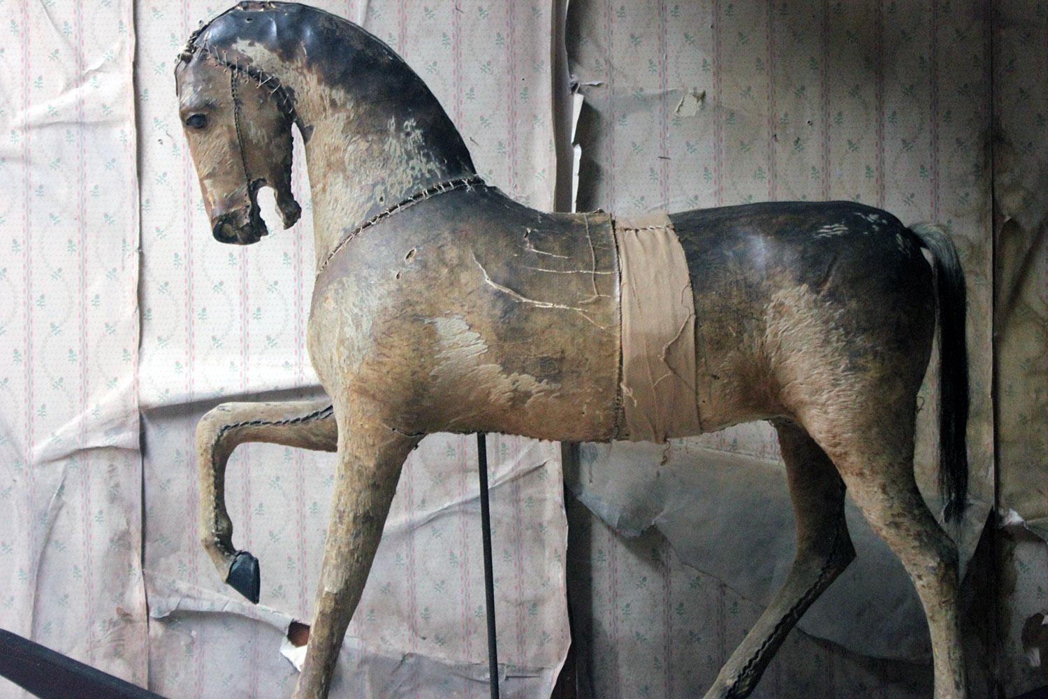 The child's two-in-one rocking and pull along horse, composed in wood and hessian and covered in its original horse hide covering with hair tail, having glass eyes and modeled with one front foot raised, on a scarlet painted trundle base with line