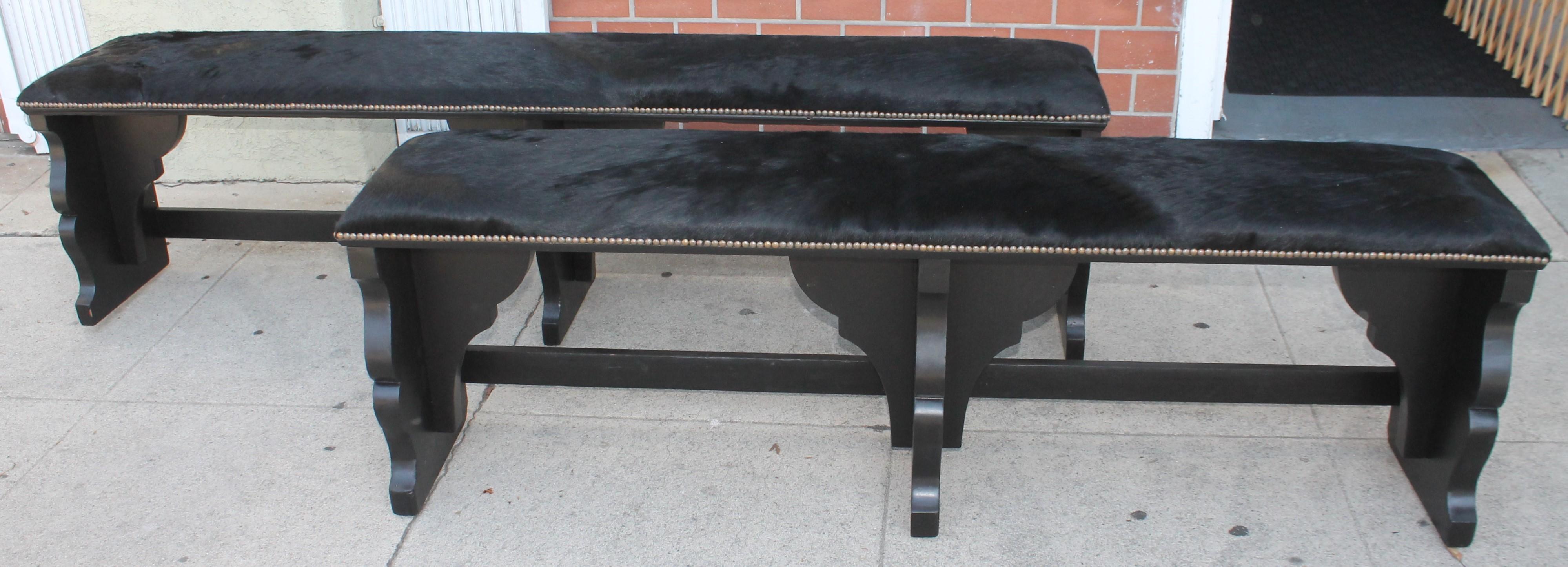 Pair of cowhide covered benches with brass tacks trim. They are painted 20Thc black paint. The two are in fantastic condition.
large Bench Measures -
81w x 14.5 deep x 21 seat height

smaller bench measures 
70w x 14 deep x 21 seat