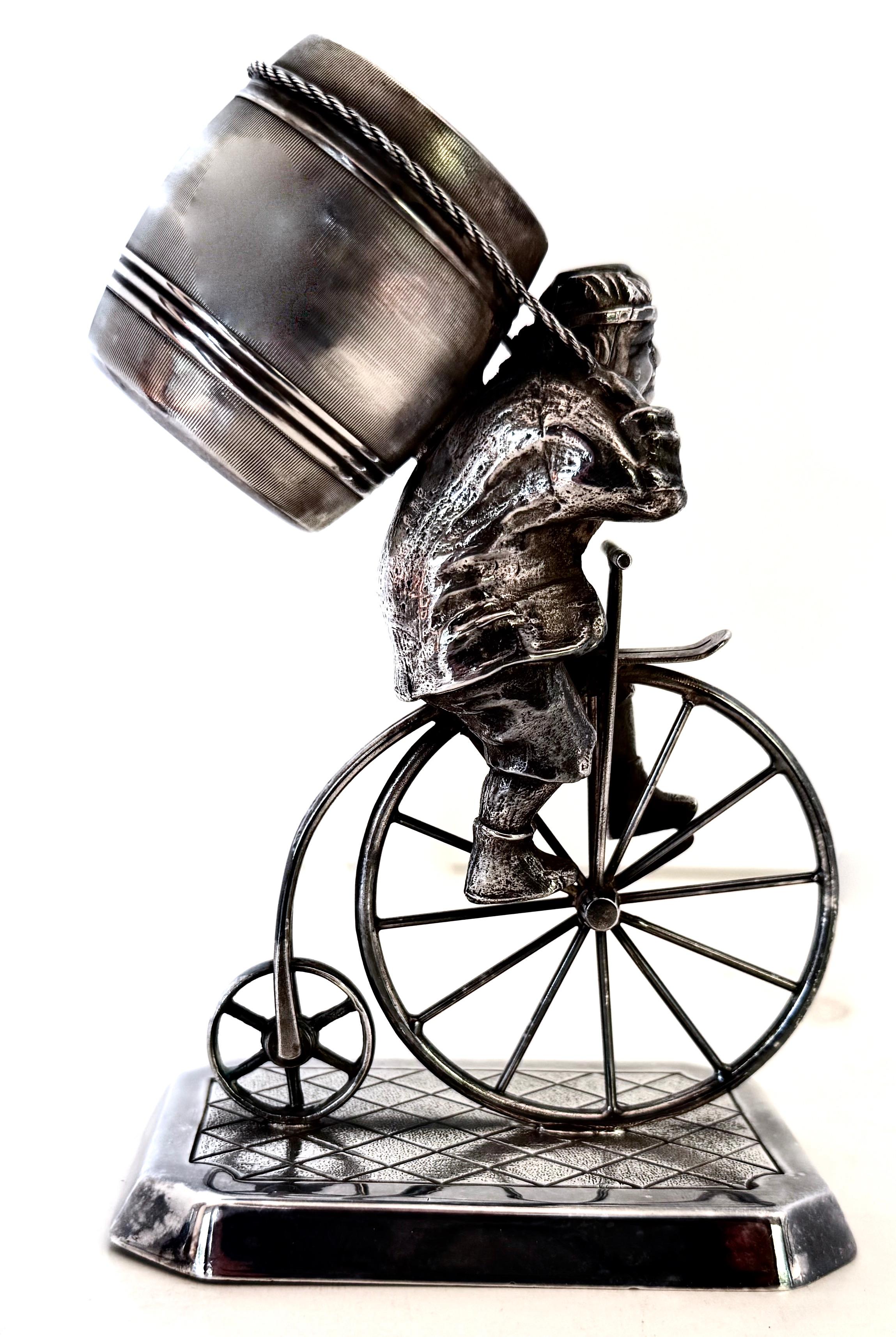 On the large side and very well made with much attention to detail, this late 19th century toothpick holder portrays a working man atop a penny farthing bicycle with a barrel strapped across his back (holds the toothpicks) mounted on a diamond