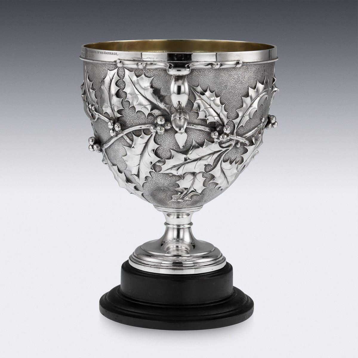 Antique 19th century Victorian solid silver skyphos cup, of traditional form on a round base, of heavy gauge and the body chased with holly leaves and berries on matted ground, flat handles with rings beneath, on a tapering foot and richly gilt