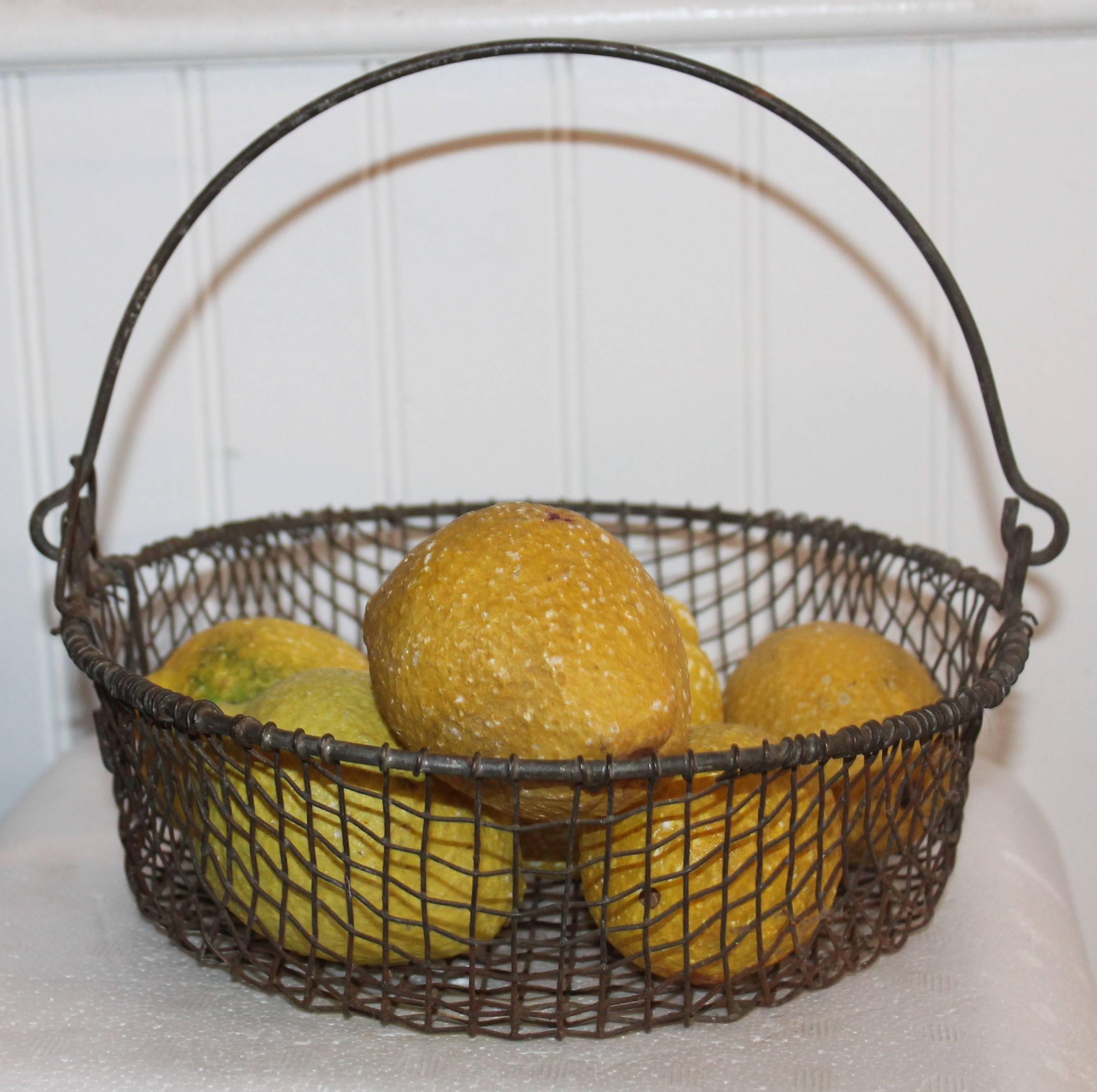 This early little swing handle wire basket is in fine condition and contains a small collection of stone or alabaster lemons.