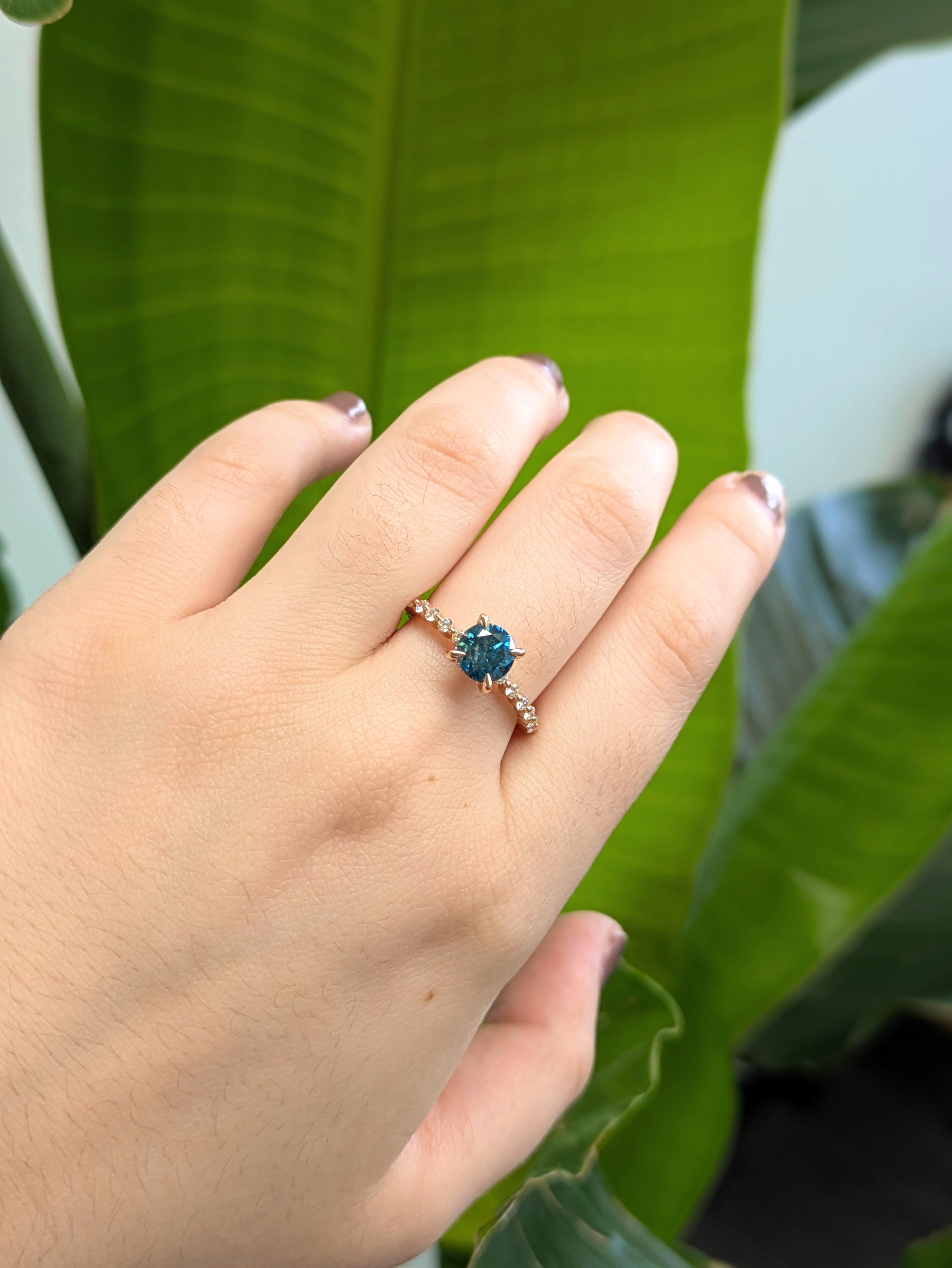 Ein atemberaubender runder blauer Diamant von 1,1 Karat steht im Mittelpunkt dieses bezaubernden Verlobungsrings, der von einem warmen Band aus 14 Karat Roségold geküsst und von funkelnden weißen Diamanten aus Erdmineralien am Schaft umarmt wird. In