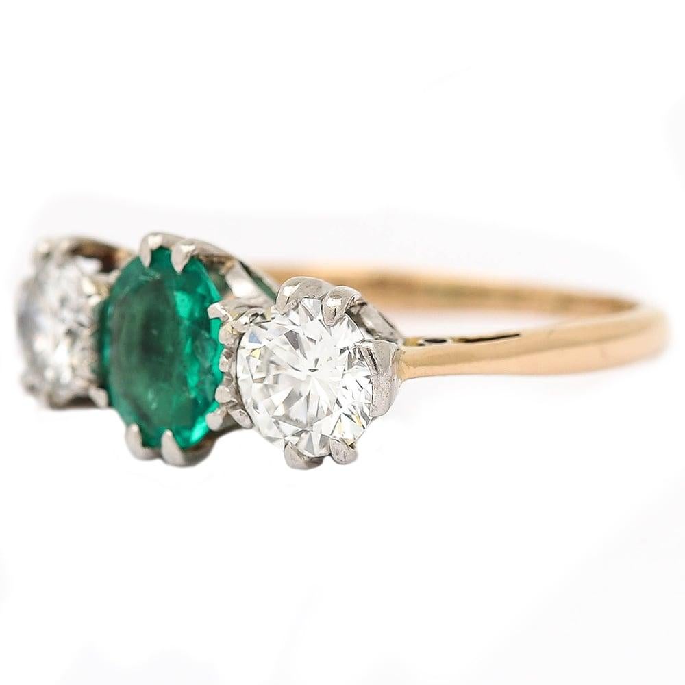 An impressive 18 karat yellow gold and platinum vintage emerald and diamond three stone ring. Comprising two round brilliant diamonds with an estimated 0.75ct weight each flank the central oval mixed cut emerald of 1ct weight (approx). Typical of