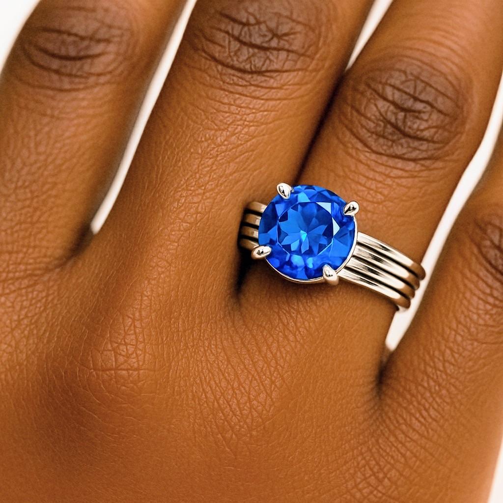 Introducing our 1ct Round Blue Topaz Platinum Silver Band Ring. This elegant piece features a stunning 1ct Blue Topaz, celebrated for its vibrant blue hue and clarity. The blue topaz is beautifully prong set in a band ring design, allowing the
