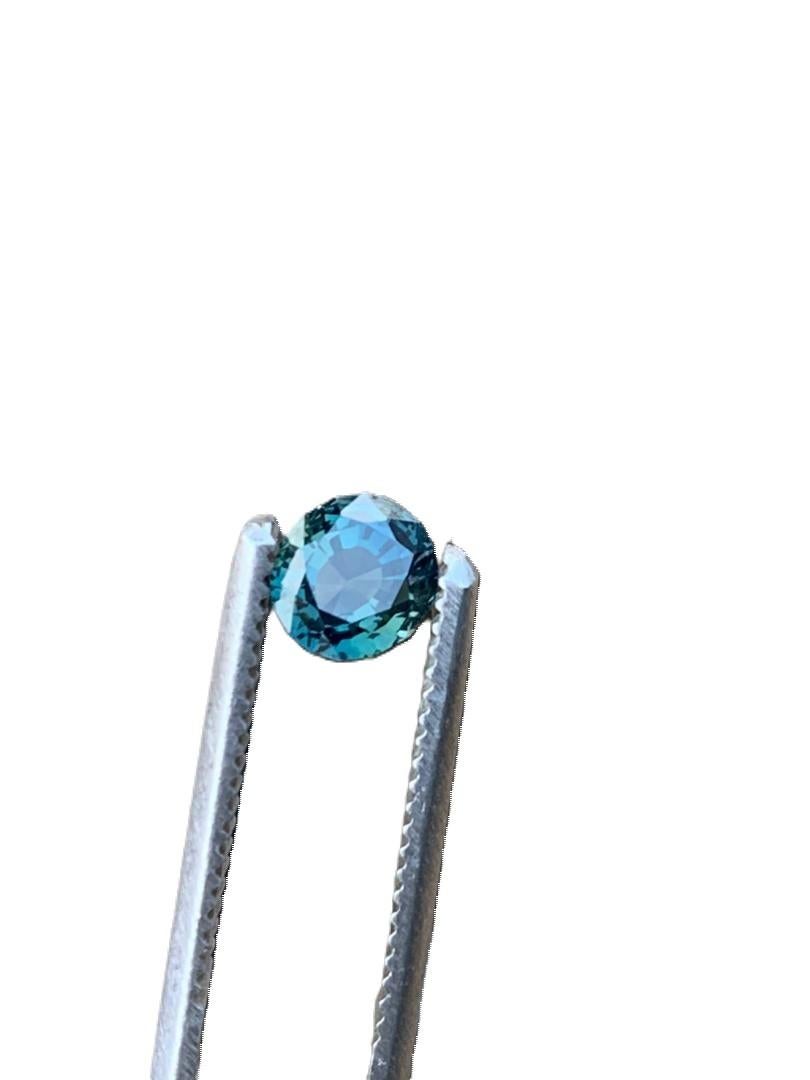 Entdecken Sie die zeitlose Schönheit dieses 1 Karat runden, blaugrünen, natürlichen, unbehandelten Saphir-Edelsteins. Sein klassischer runder Schliff strahlt mit einer Symphonie aus Licht, die die tiefblaue Farbe des Steins hervorhebt, die die