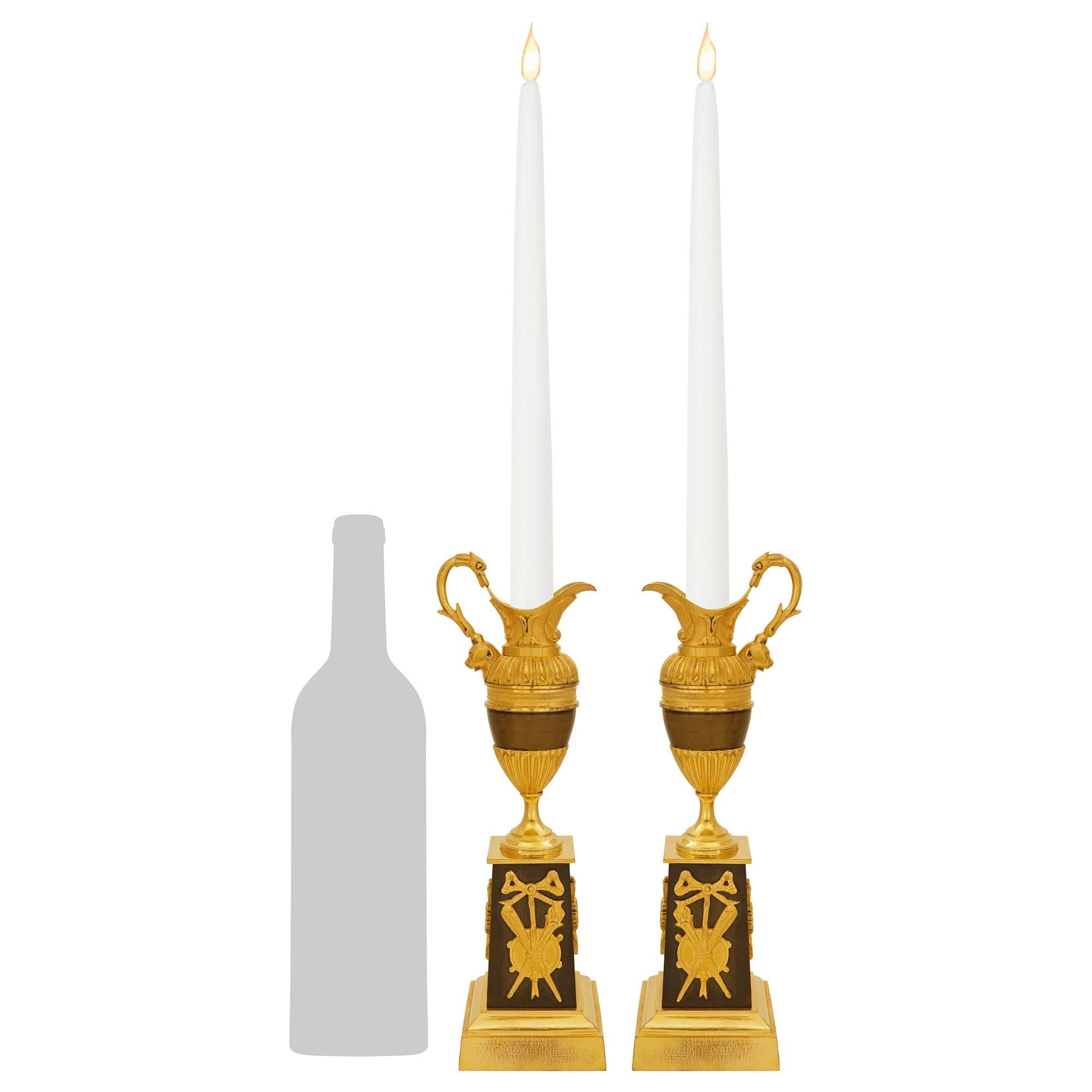 An attractive and high quality pair of French early 19th century 1st Empire Period patinated Bronze and Ormolu candlesticks, circa 1805. This wonderful pair of ewer designed candlesticks are raised by square mottled Ormolu plinths below a square