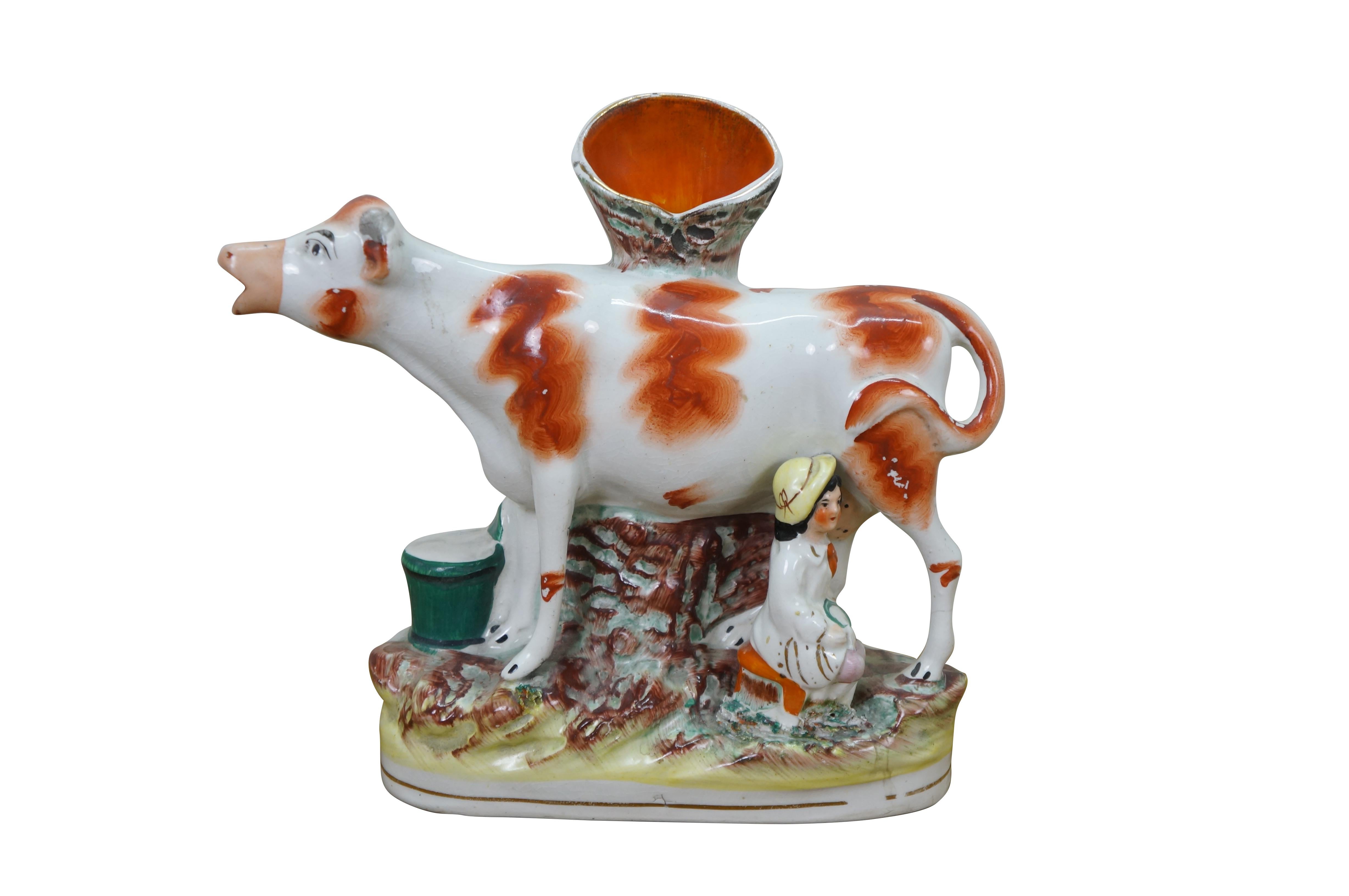 Paire de figurines de vase à bec plat en porcelaine de Staffordshire de la fin du XIXe siècle représentant des vaches rouges et blanches, debout près d'un tronc d'arbre et traites par des laitières avec des seaux verts.

Dimensions :
9,5
