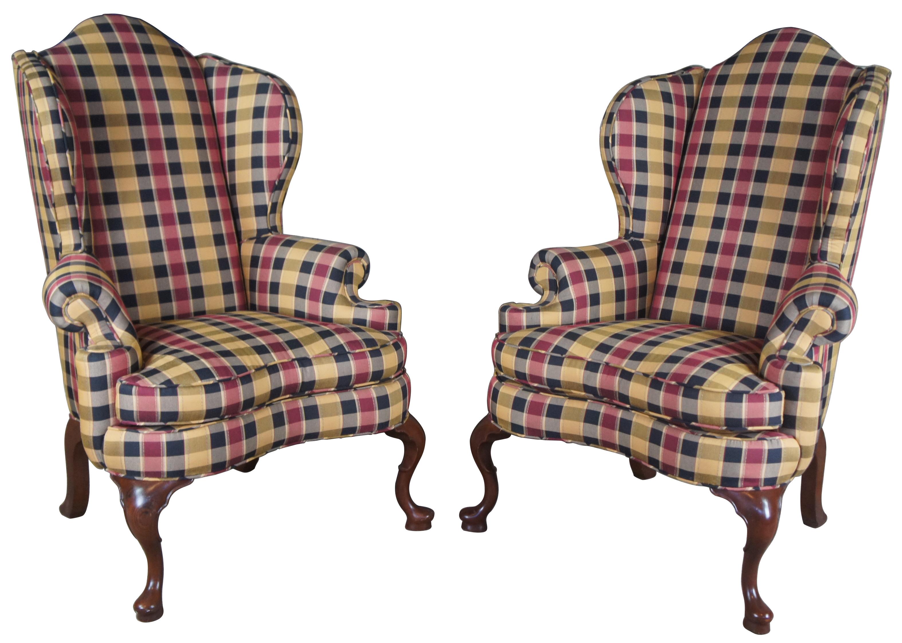 Pair of two mid century oversized wingback chairs. Made of mahogany with a wide stance, accented with rolled arms, camel back top and scrolled legs. Finished in a yellow, blue, grey, and red Ralph Lauren style plaid upholstery.
   