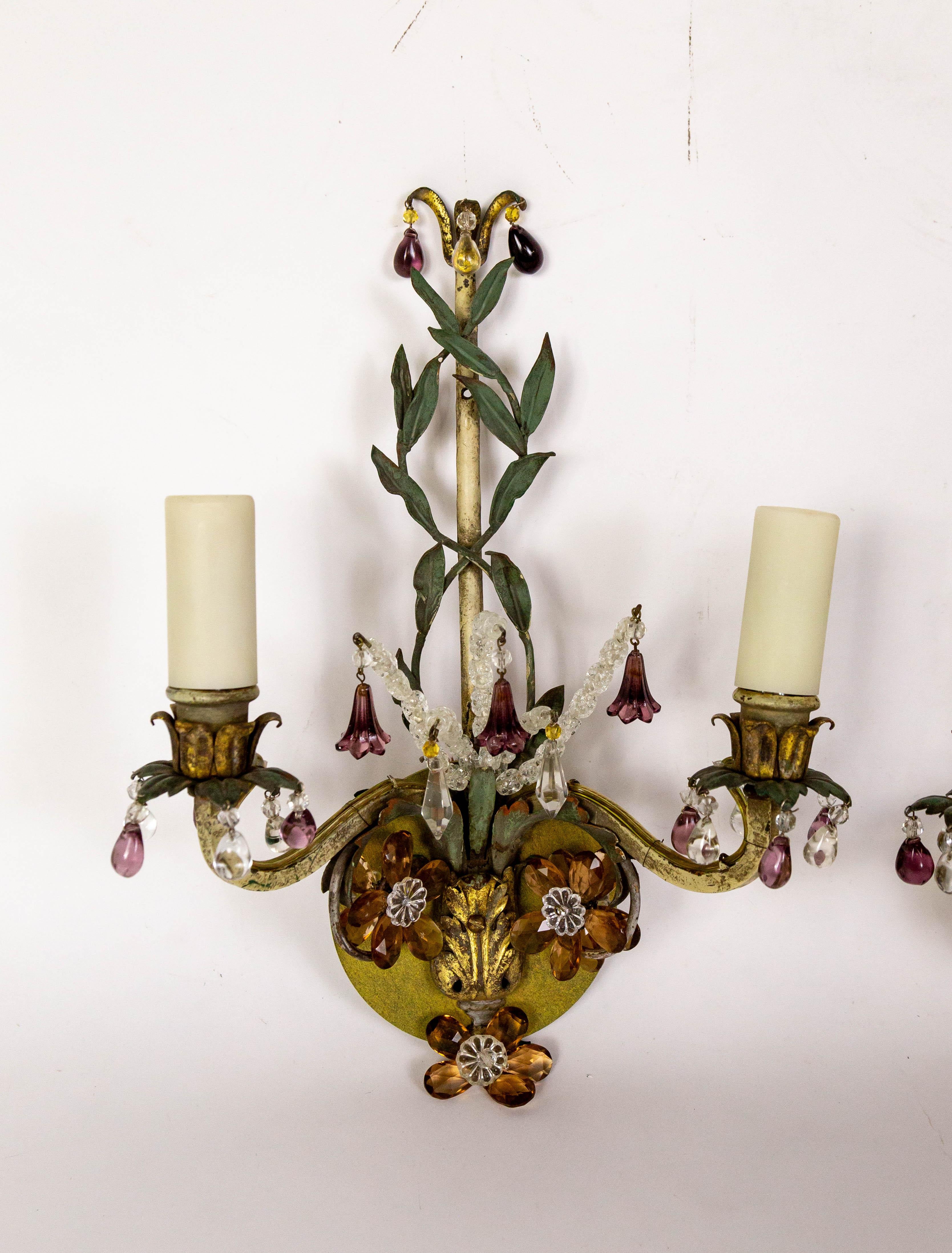 This pair of elegant, 2-arm, polychrome candelabra sconces with various finishes-green, gold, white gold, and brass, were created in the early 20th century.  The structure has intertwining green vines and is adorned with amethyst, clear, and amber