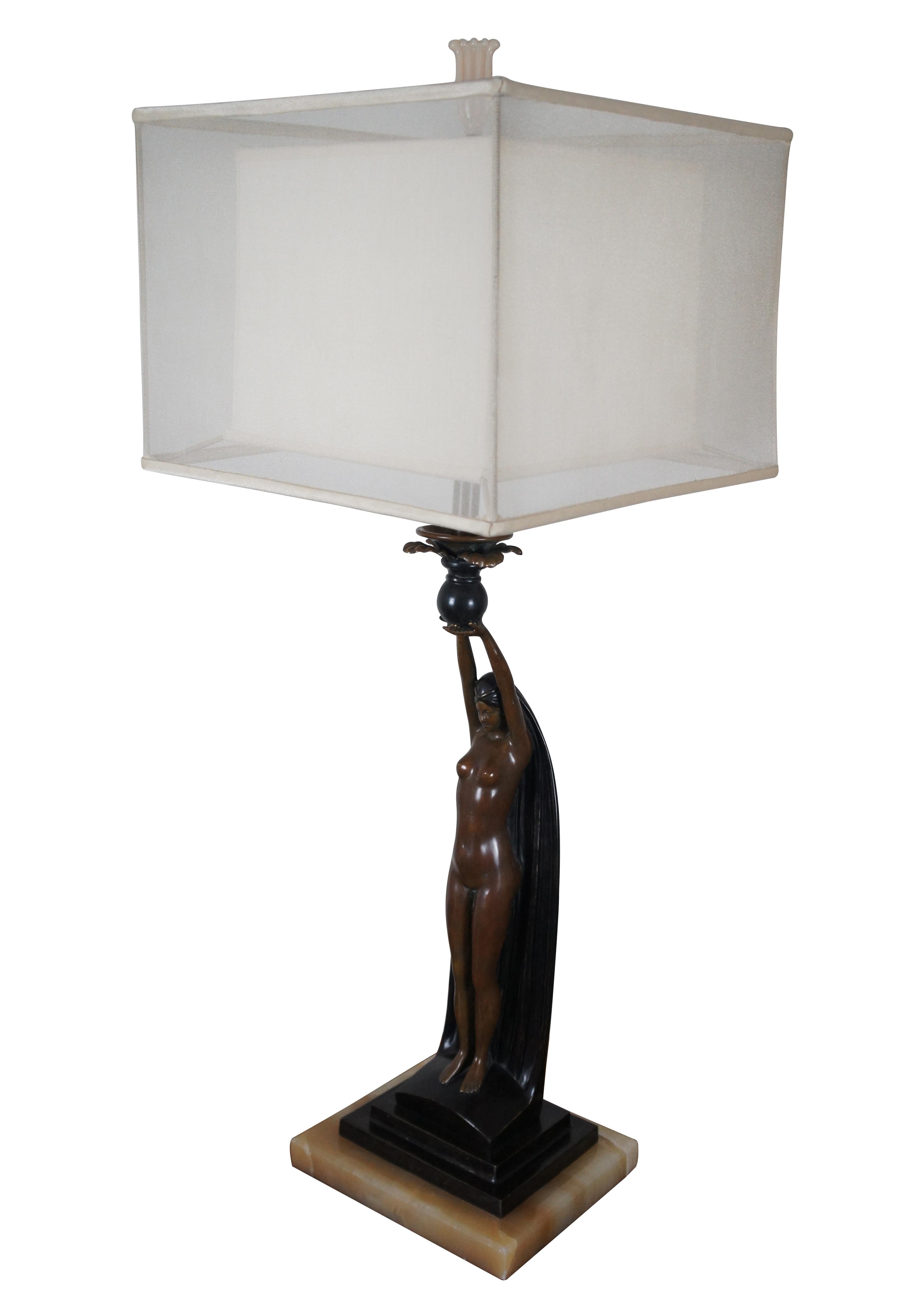 An impressive pair of table lamps featuring heavy bronze Art Deco female nude figures lifting vases topped with leaves, standing on tiered plinths with white marble bases. These stunning lamps are finished with Art Deco era flower shaped glass