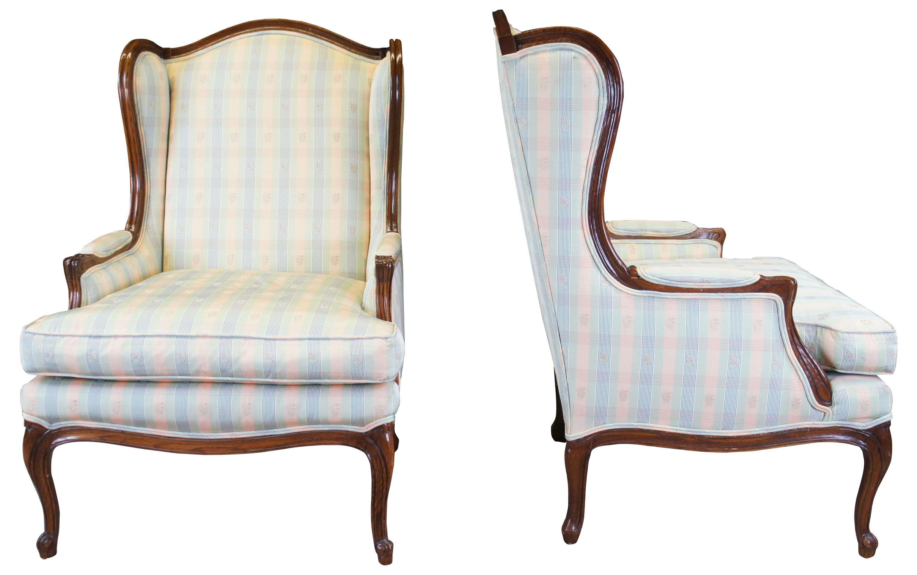 A beautiful pair of French Bergere wingback chairs by Baker Furniture, circa 1970s. Made from oak with a camelback leading to contoured sides and padded arms. The chair is supported by cabriole legs with scrolled feet along the front. Upholstered in
