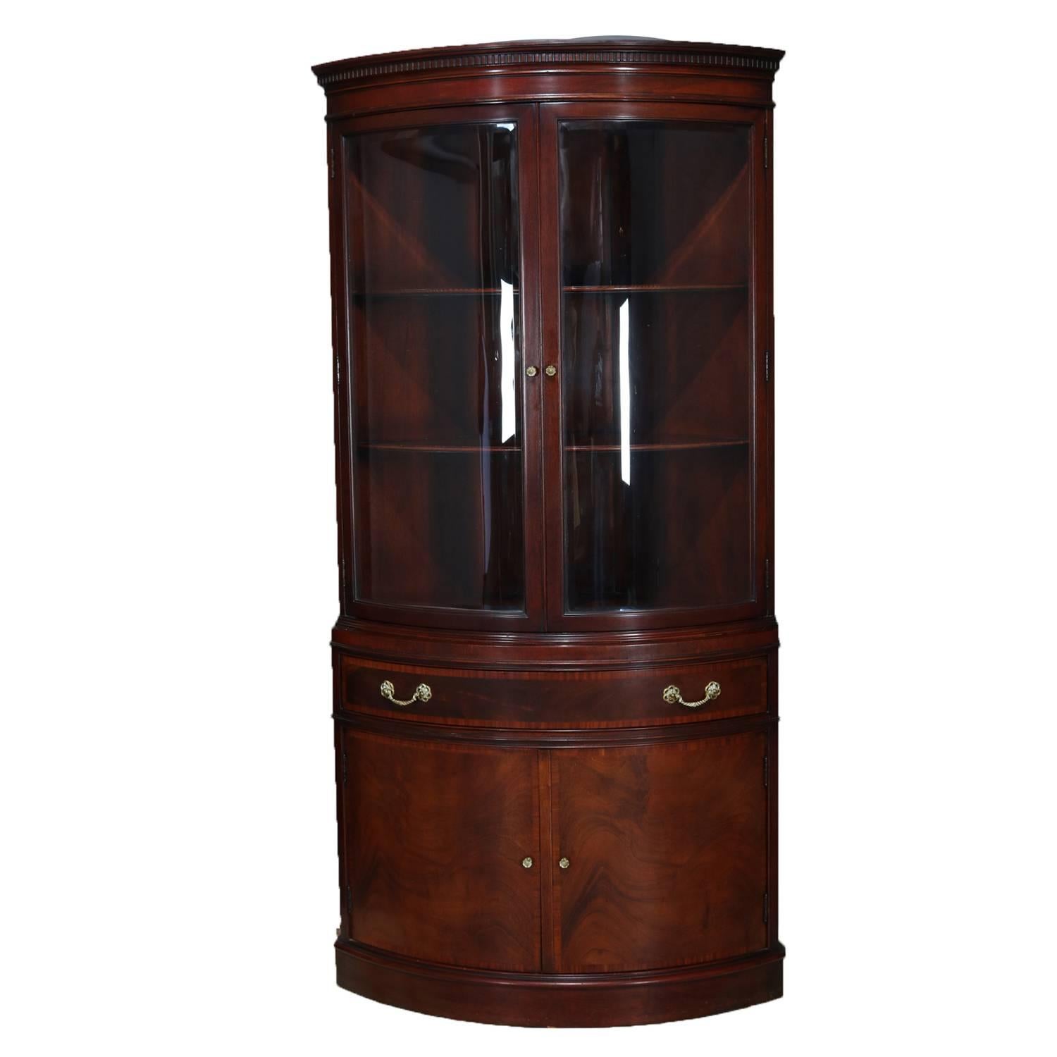 Pair of Baker School flame mahogany corner cupboards by Fancher, NY feature half round form each with double curved glass upper doors opening to fixed shelf interior over single long drawer and seated on double door lower cabinet, elements include