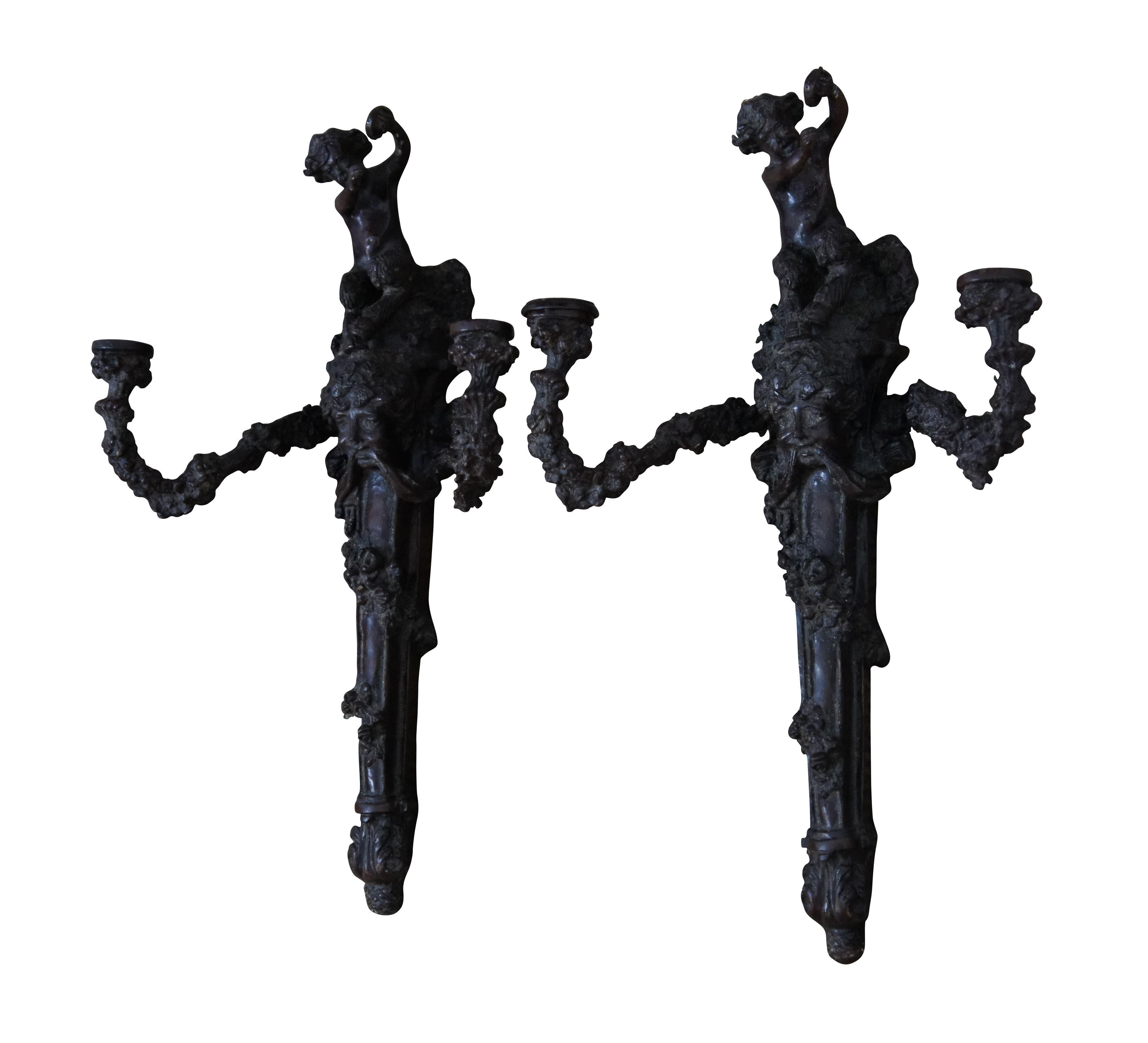 Pair of late 20th century heavy bronze two arm candelabra wall sconces. Torchiere style wrapped in flowering vines branching off a Dionysus / Bachhus style head and topped with a small faun / Pan-like figure beating a small drum or tambourine.  Hand