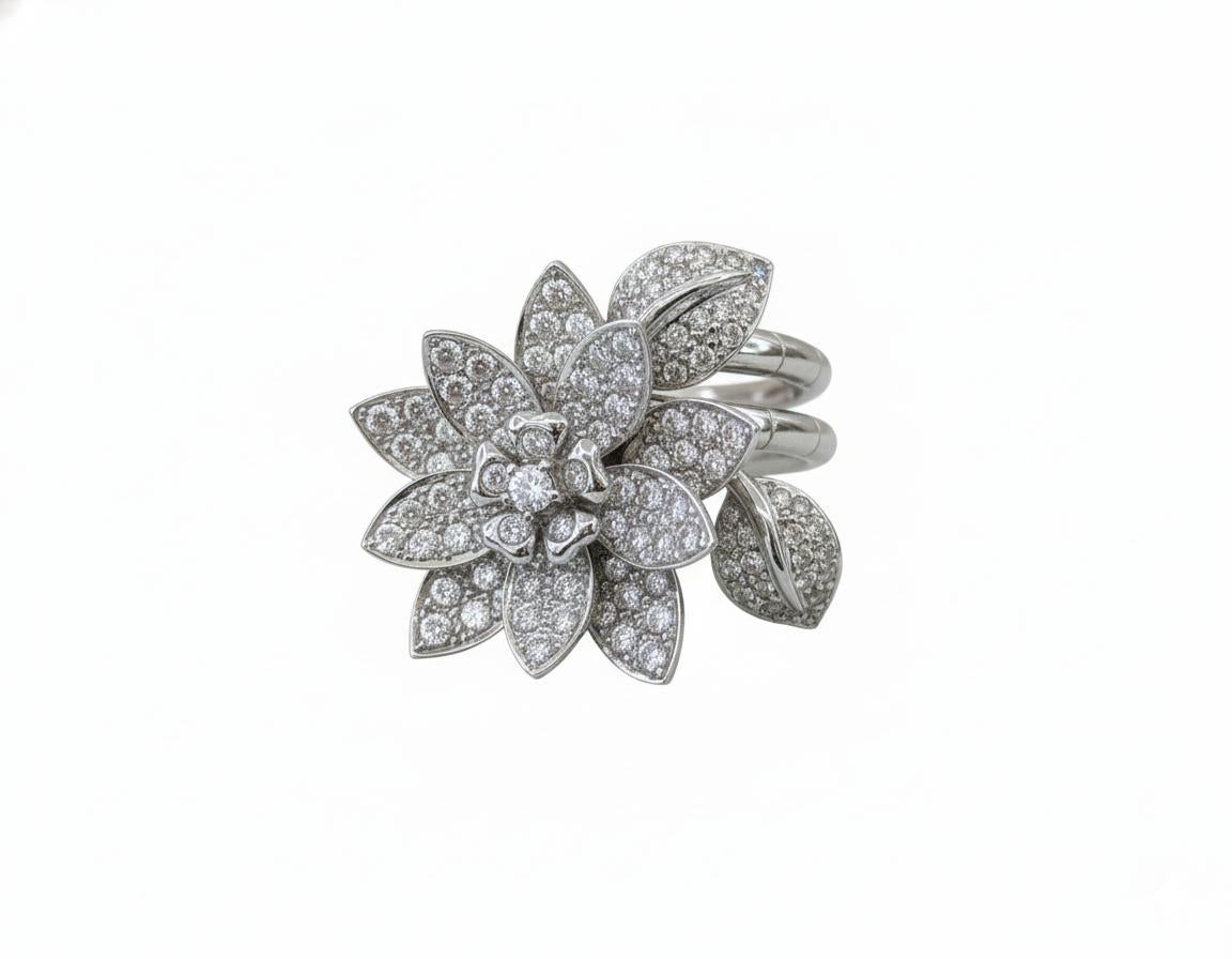 Ein auffälliger und kunstvoller Ring in Form einer blühenden Lotusblume, gefertigt aus massivem 14-karätigem Weißgold, der zwischen den Fingern getragen wird.

Im Mittelpunkt steht ein natürlicher runder Brillant, umgeben von 116 kleineren runden