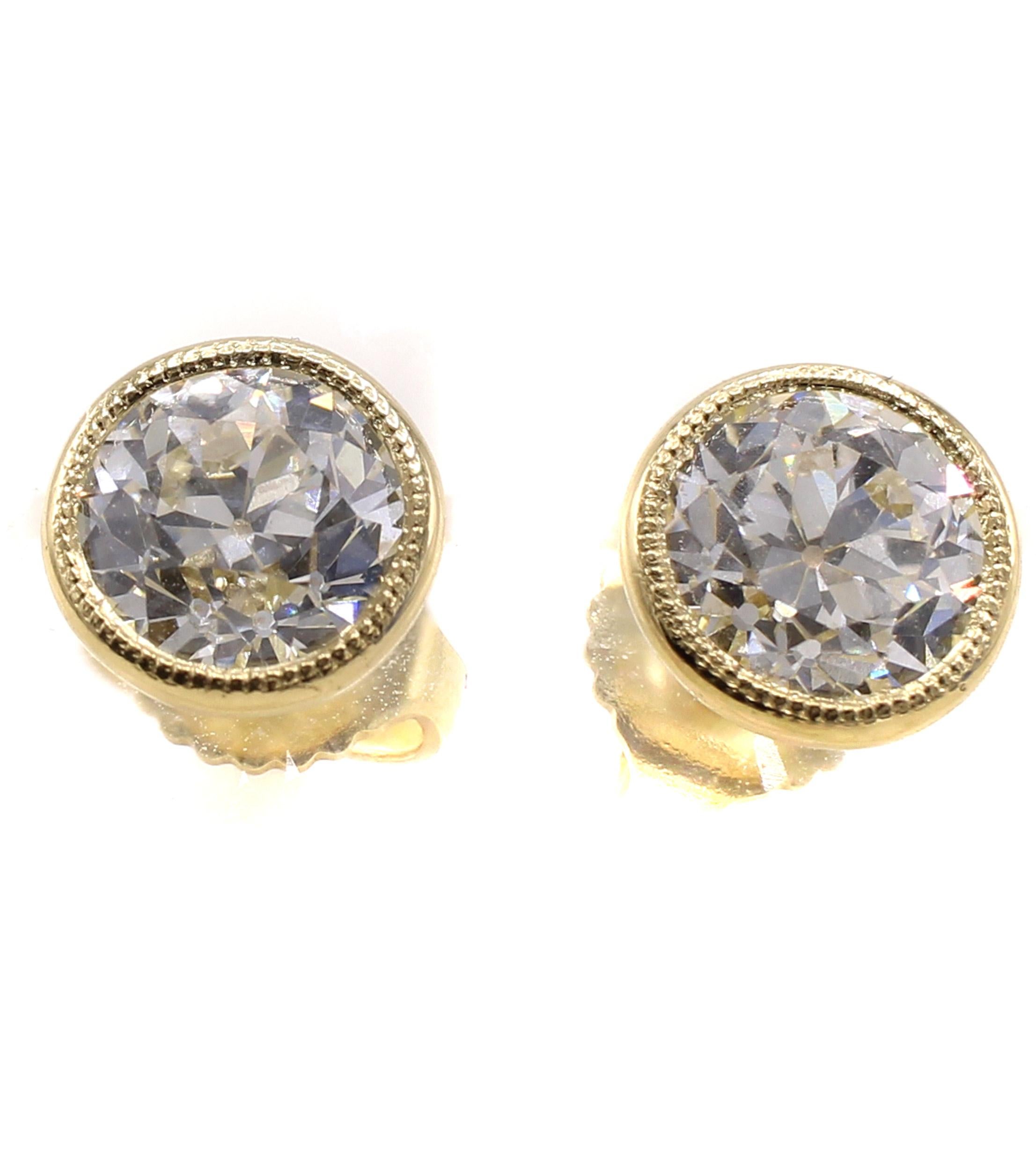 Two charming Old European Cut diamonds with a total weight of 2 carats have been set into these handcrafted 18 karat yellow gold bezel set mountings. The tops of the bezels have fine milligrain work combining the new world with the old cuts from a