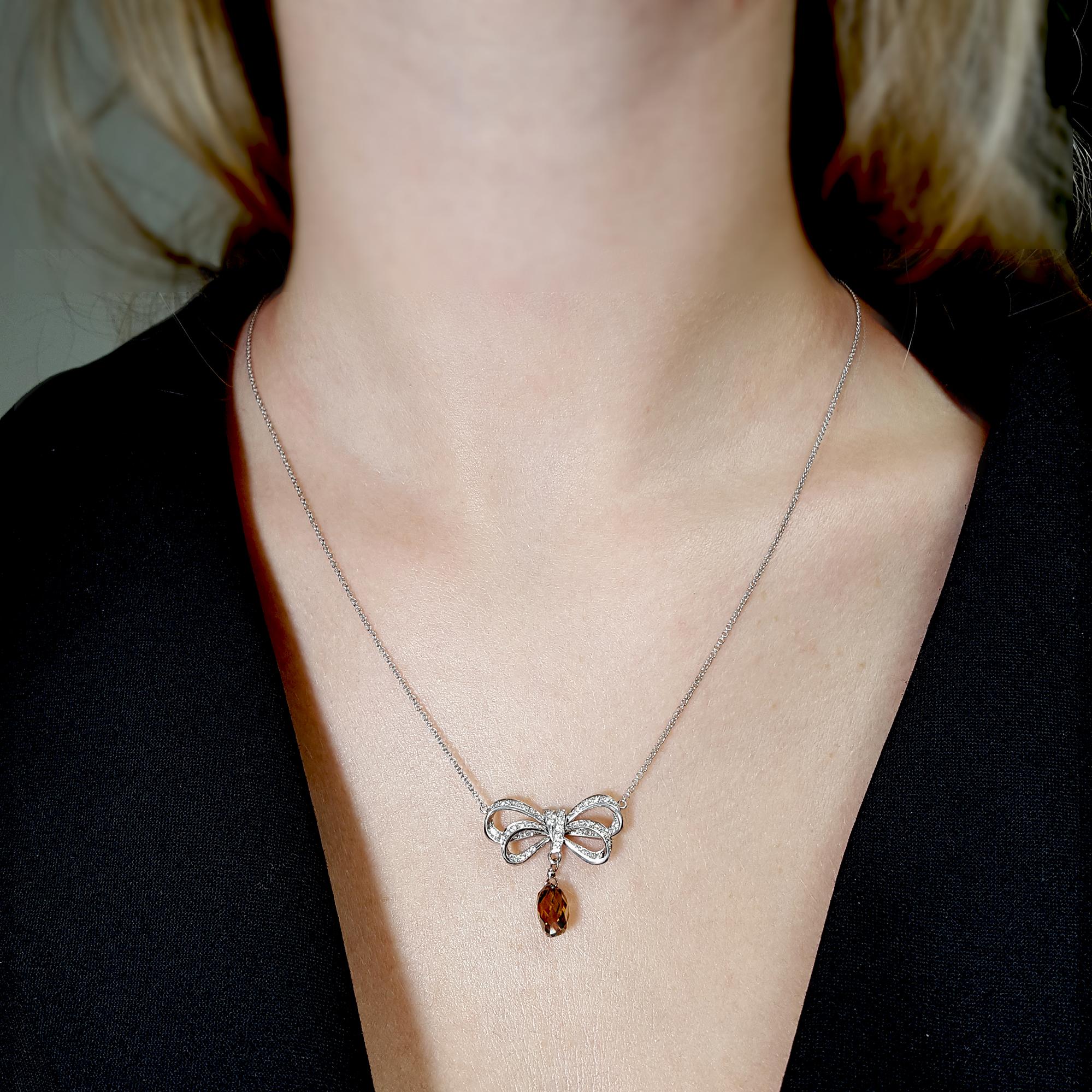 Introducing a captivating pendant necklace featuring a bow-inspired open-style design, adorned with a central 2.21-carat Briolette-cut Fancy Dark Orangy Brown diamond certified by GIA. This remarkable centerpiece is encircled by 51 round brilliant