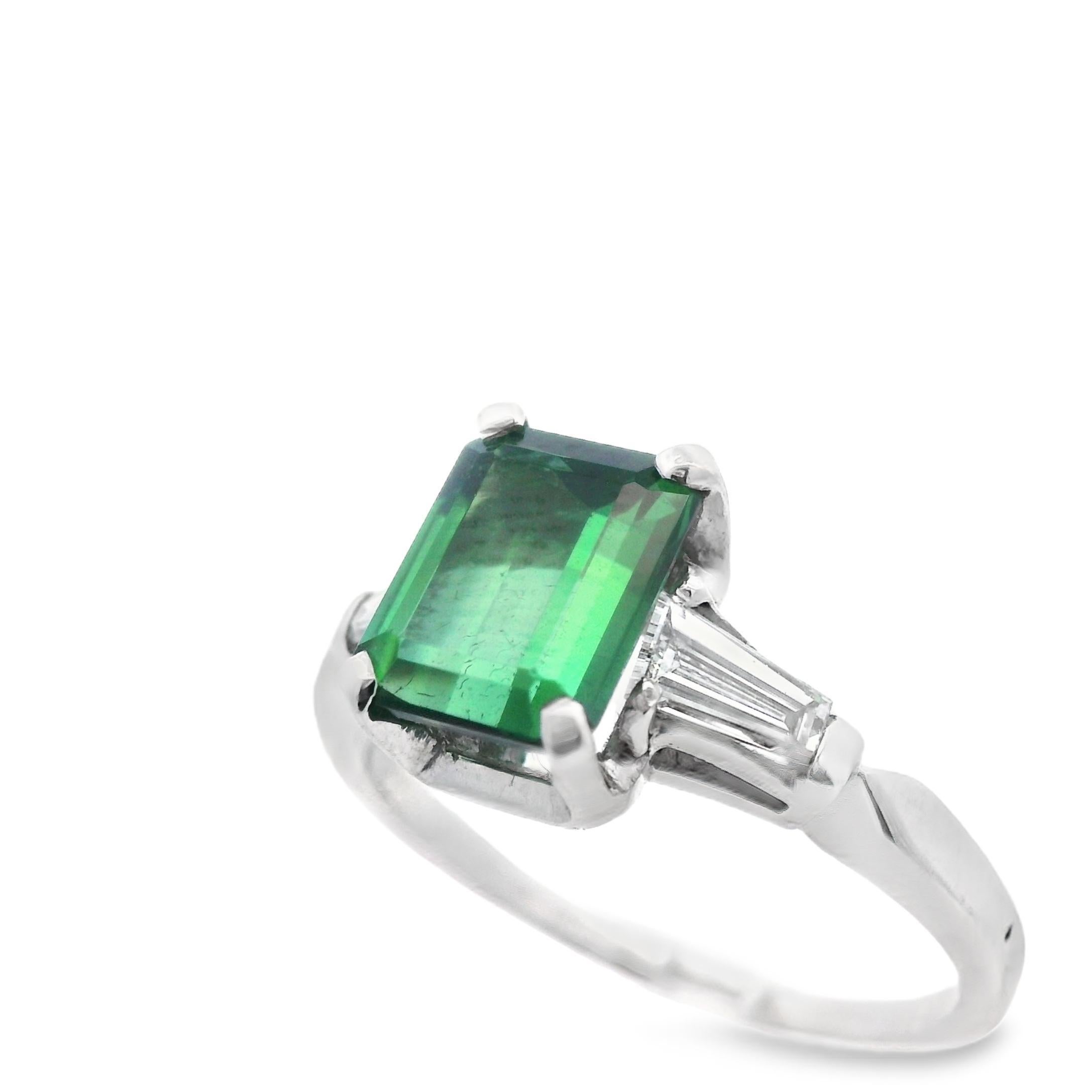 Cette magnifique bague en platine est ornée d'une tourmaline verte de taille émeraude au centre et de diamants baguettes effilés sur les épaules. La riche tourmaline verte a une teinte profonde et est incroyablement bien taillée, créant un aspect