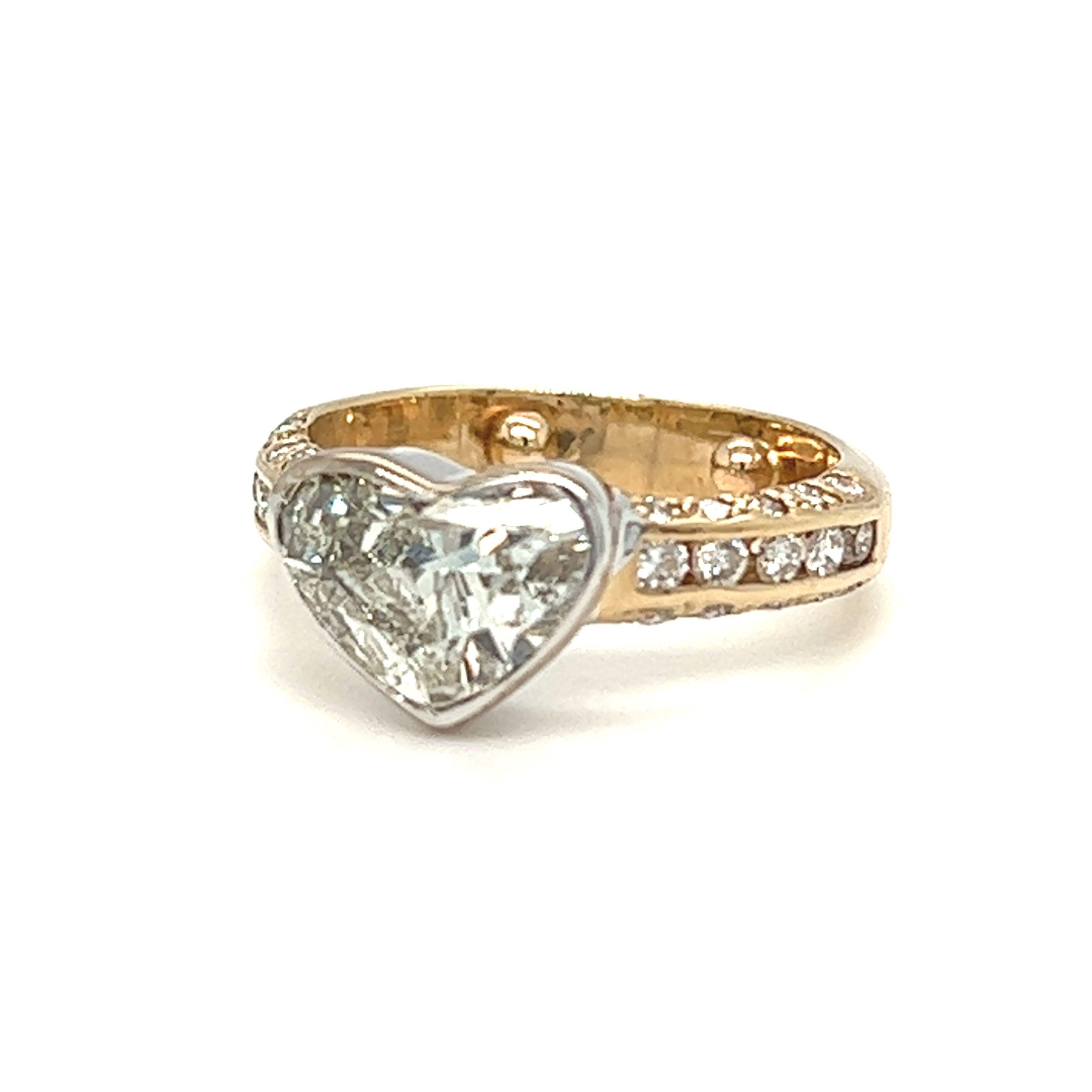 From our estate jewelry collection is this elegant yet playful ring features a grayish heart shaped diamond weighing approximately 2 carats resting within a sleek bezel frame. Accenting this heart shaped diamond center stone is an ensemble of
