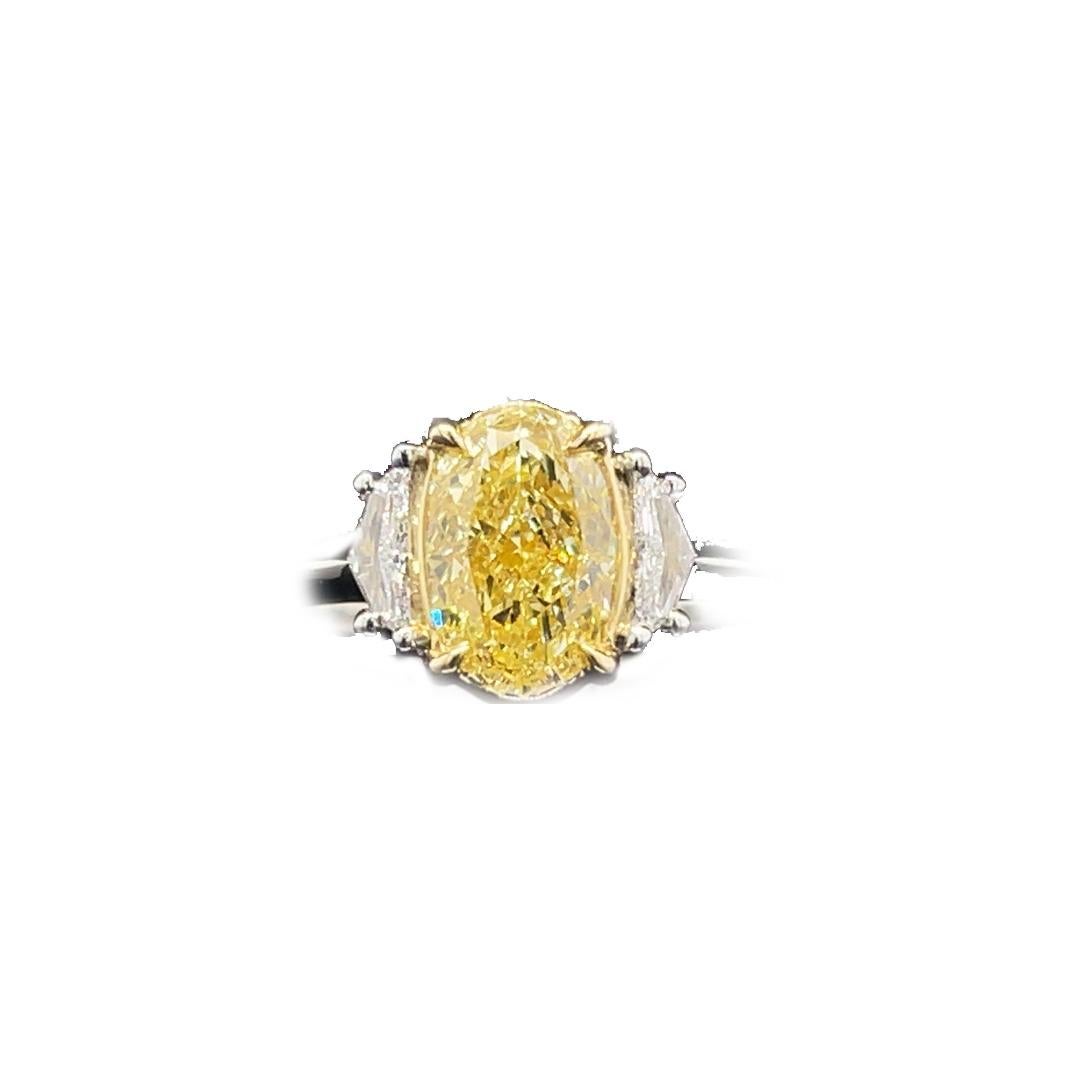 Cette bague de fiançailles à trois pierres présente un diamant ovale de 2 carats de couleur jaune fantaisie. La GIA a certifié ce diamant comme étant de pureté VS2. Les pierres présentent un excellent poli et une très bonne symétrie, ce qui garantit