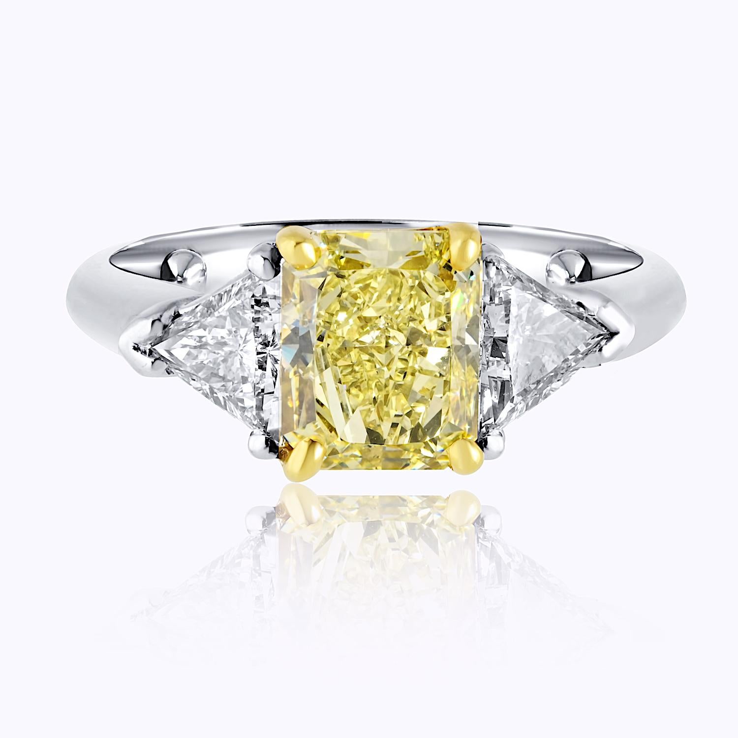 This elegant three-stone engagement ring features a stunning 2.01-carat radiant cut diamond with a captivating fancy yellow hue and VS2 clarity, certified by GIA. 

GIA#2135010585.

Complementing the center stone are two beautifully matched