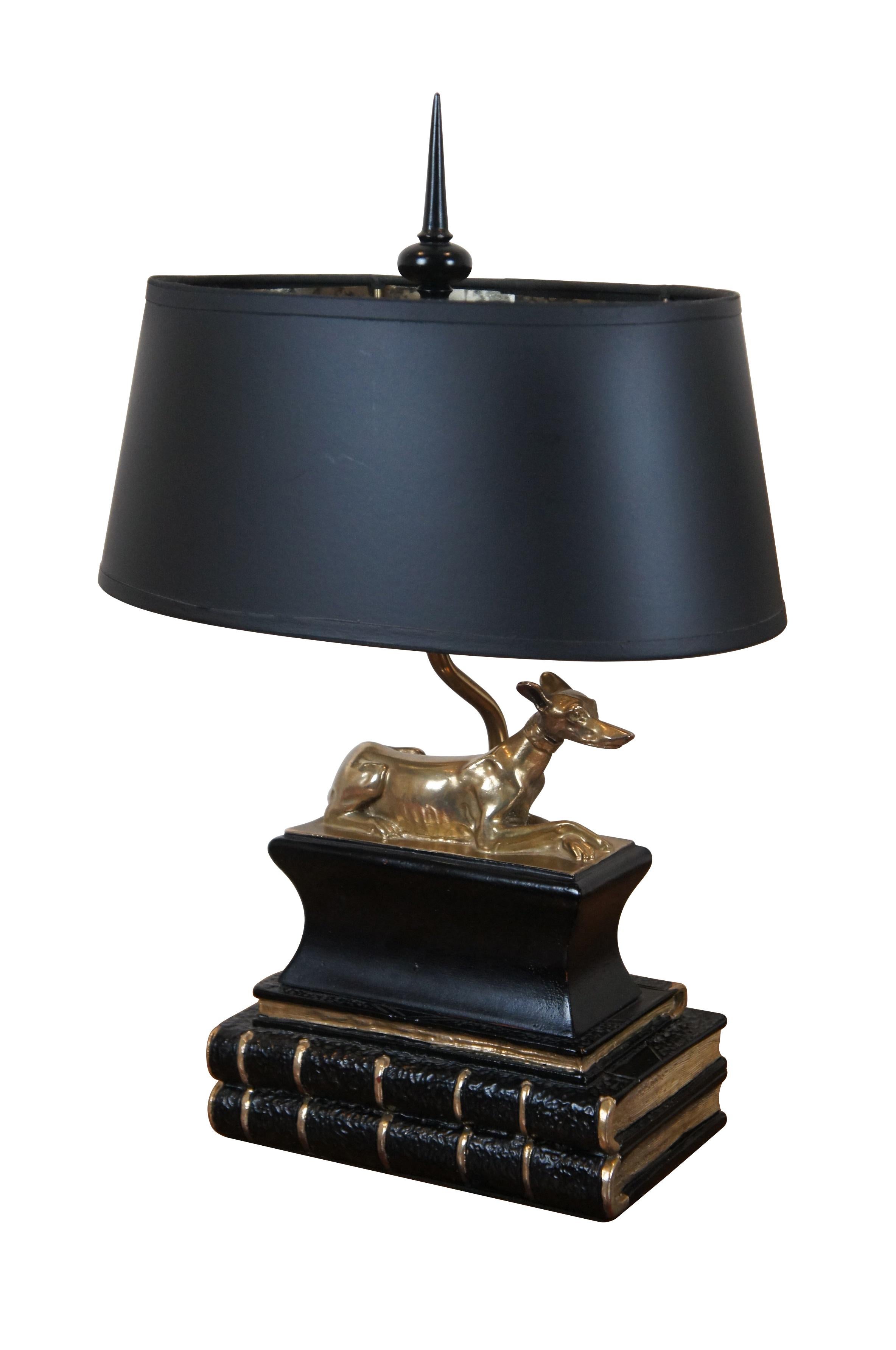 Vintage 1973 Chapman Manufacturing Company table lamps. Composite material showing dogs (whippets) reclining on a plinth, perched on a small stack of books, finished in black and gold. Includes spear shaped finials and black paper shades with foiled