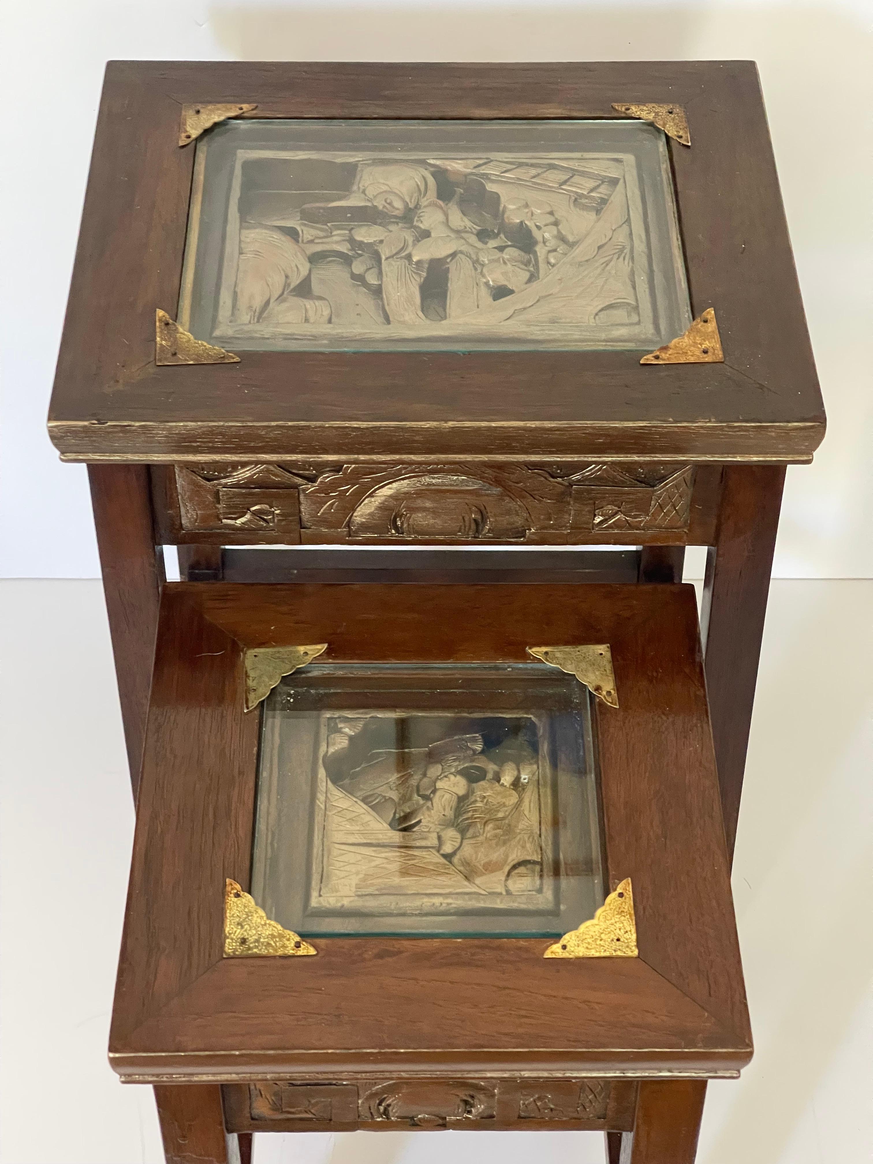 Two antique Chinese Nesting tables of stands. Hardwood carving tops and sides with gold bronze wash.. Protected with glass.