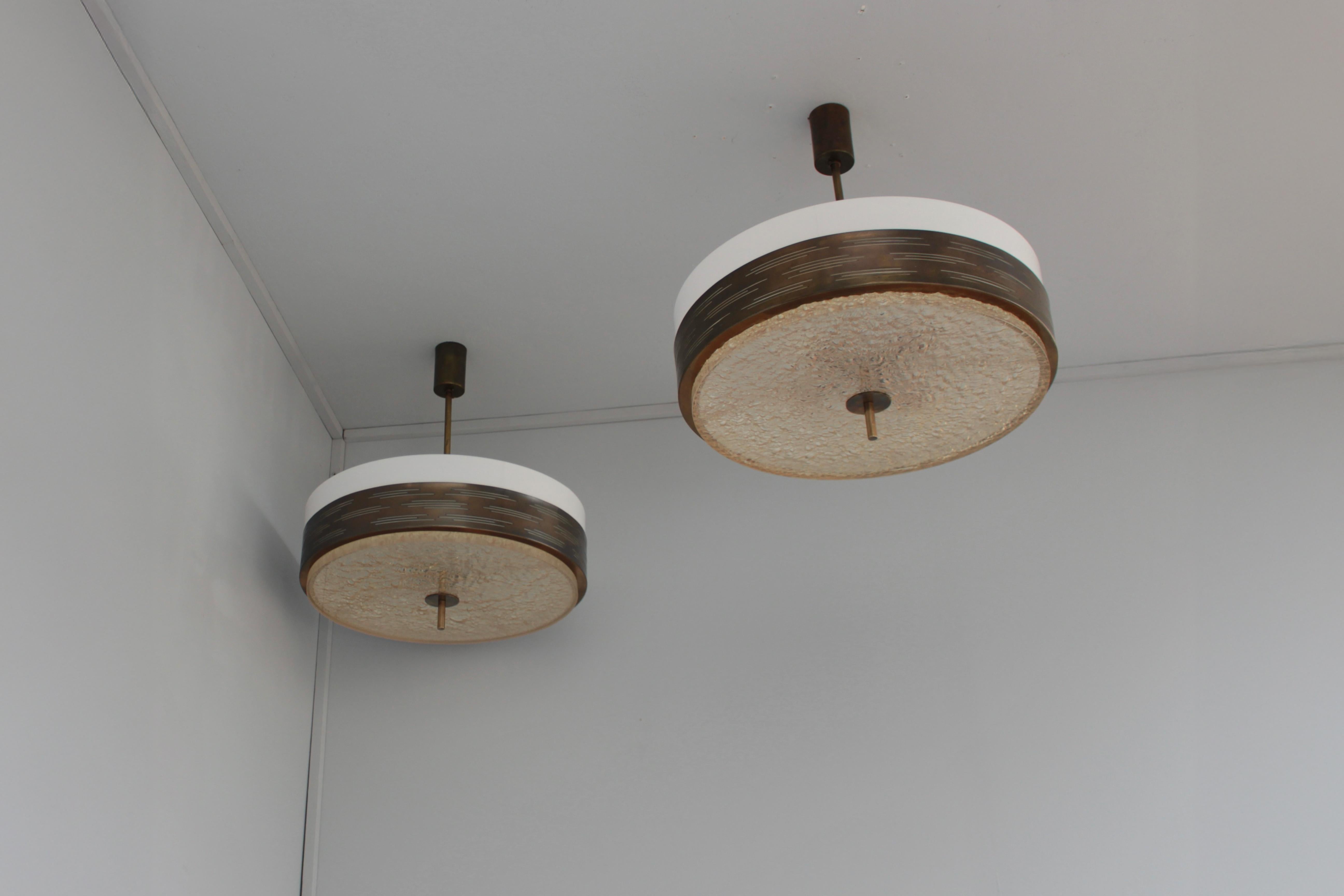Due raffinati pendenti rotondi francesi del Mid-Century con una struttura in metallo patinato e perforato che contiene una lastra Dallux e diffusori laterali in Perspex.

Il prezzo si intende per ciondolo.