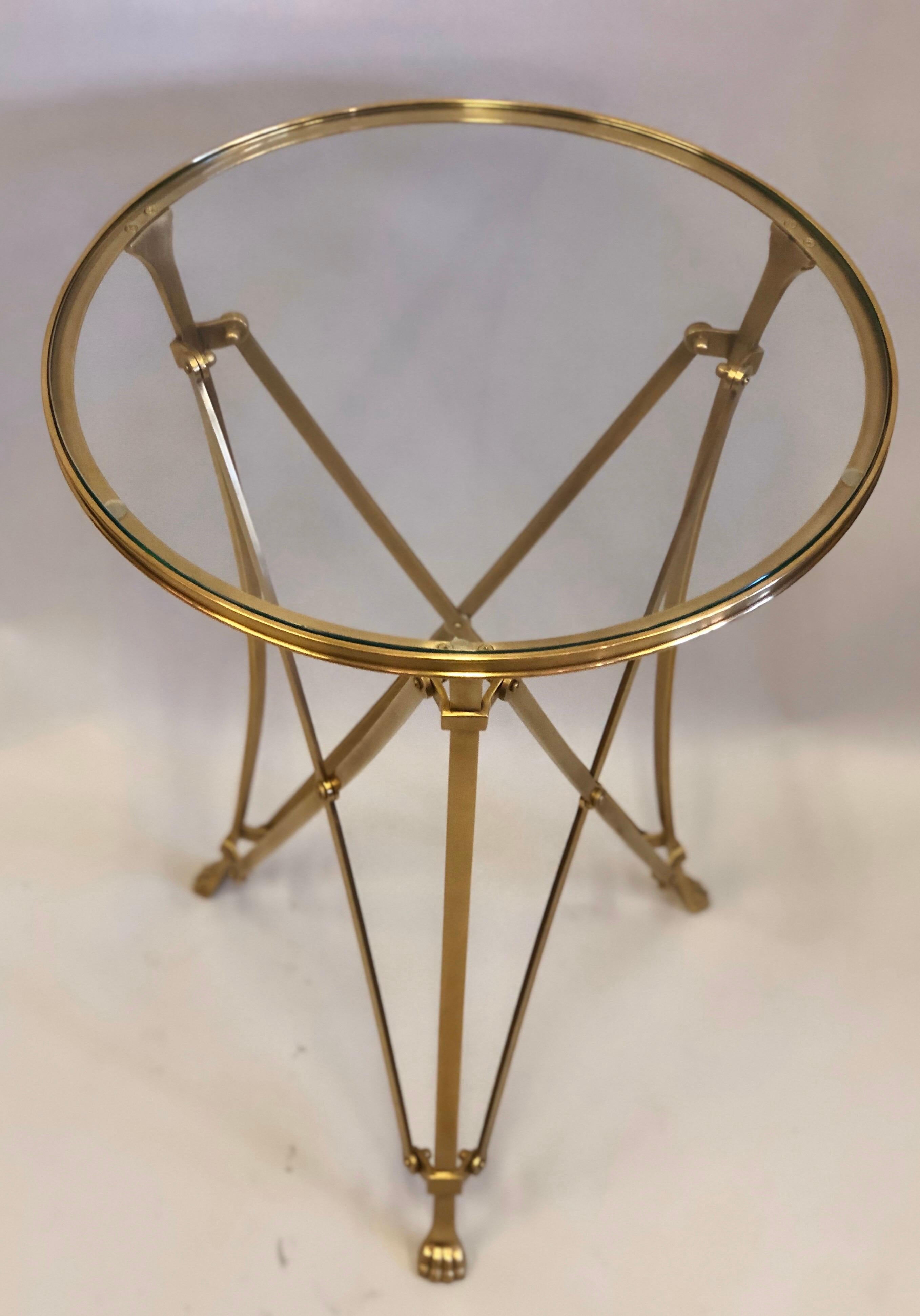 Elegant pair of French modern neoclassical inspired side tables or gueridons in solid brass with refined detailing present in legs, feet, cross-bracing and hardware. The top is tempered glass and has a slight bevel. Highest quality of design,