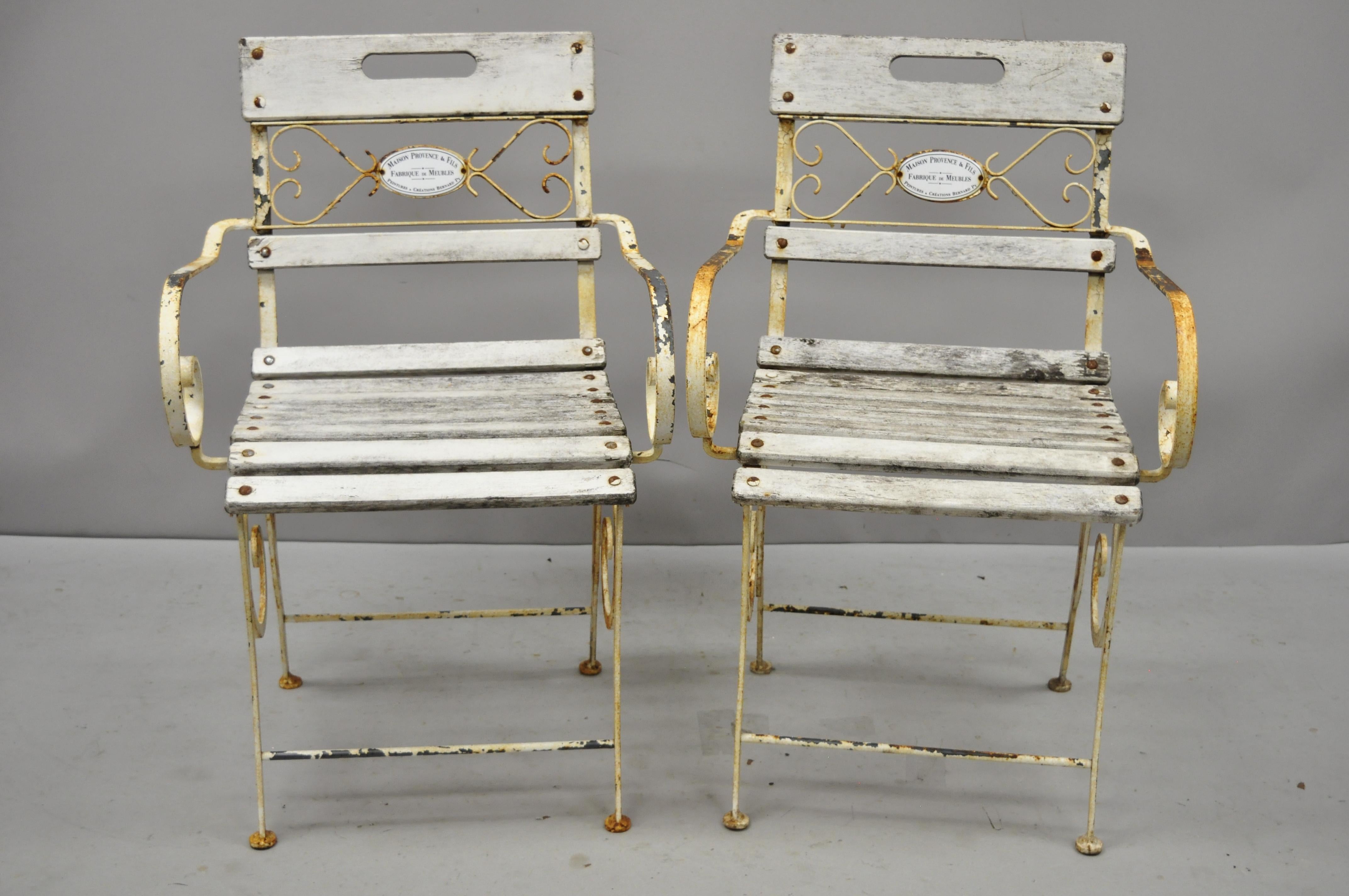 Pair of Vintage French Victorian Wrought Iron and Wooden Slat Seat Garden Arm Chairs by Maison Provence & Fils. Item features scrolling wrought iron frames, wooden slat seats, porcelain enamel plaque to back which reads 